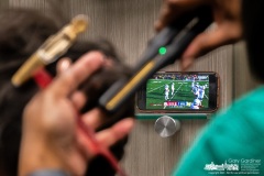 A stylist and her client engage in multitasking at a salon by simultaneously watching the Ohio State-Michigan game on a cellphone propped on a shelf in the styling booth during the hair appointment.  My Final Photo for November 25, 2023. 