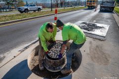 Workers replace a manhole cover after completing the drilling for a concrete surround and raising the manhole to the height of Sunbury Road. My Final Photo for November 16, 2023.