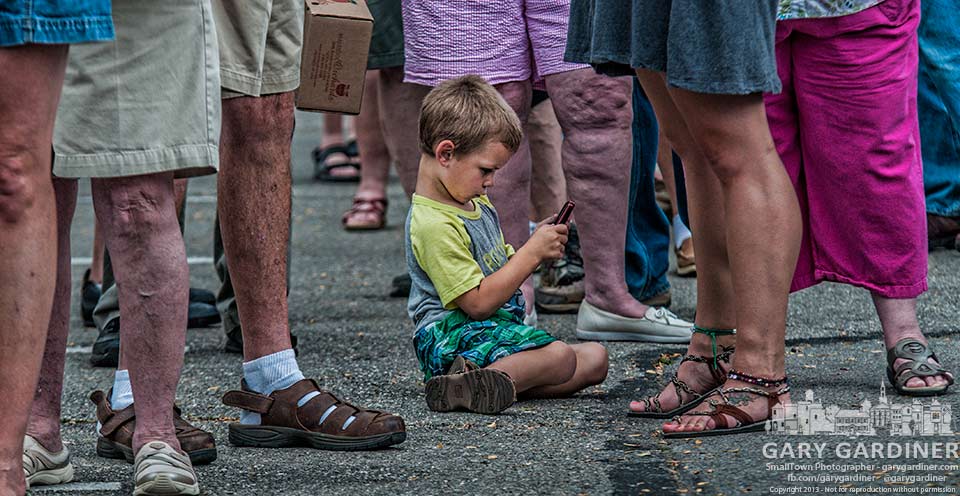 A young boy entertains himself with a smartphone game as he sits in the long line of people waiting to buy peaches at the Uptown Westerville Farmers market. My Final Photo for Aug. 28, 2013.