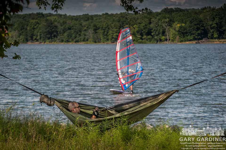 A cyclist takes a break in his lightweight hammock stretched between two trees on the shore of Hoover Reservoir as a sailboarder runs in the wind. My Final Photo for Aug. 4, 2013.
