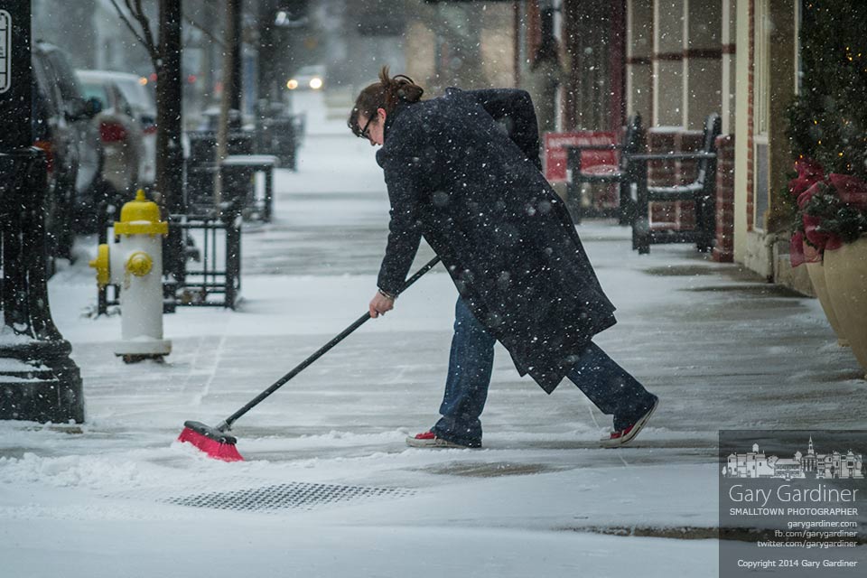 Hannah Forbus uses a wide push broom to clear snow from in front6 of Ohio art market in uptown Westerville as a storm began to leave a layer of snow in the city. My Final Photo for Jan. 16.