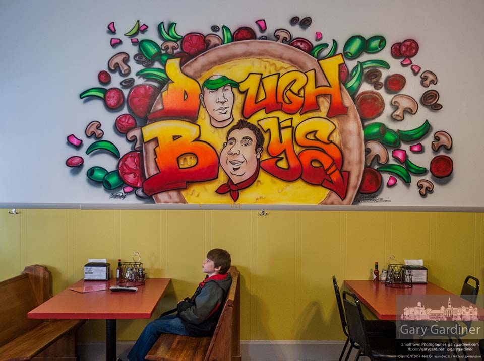 A young customer waits at a table beneath the new logo painted on the wall of Doughboy's Pizzeria while his family at other tables prepares their orders. My Final Photo for Feb. 15, 2014.