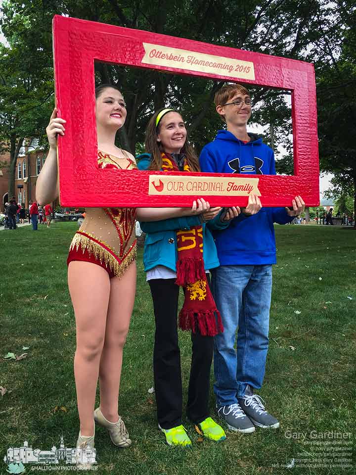 An Otterbein Dance Team member stands on her tiptoes as she poses with two others for photos inside a wooden frame after the homecoming parade. My Final Photo for Sept. 26.