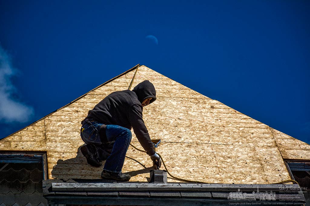 A roofer scrapes away old shingles on the roof of Flowers by Doris as a quarter moon rises in the sky behind him. My Final Photo for April 12, 2016.