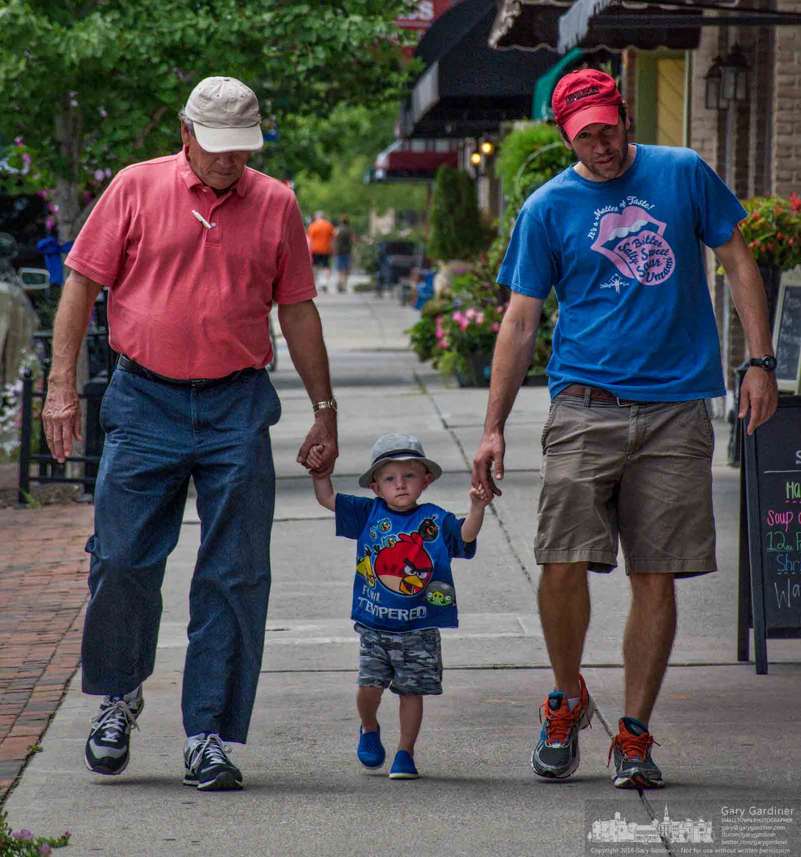 Grandfather, father, and son, all wearing hats against the afternoon heat, hold hands walking down the sidewalk in Uptown Westerville Friday. My Final Photo for August 12, 2016.