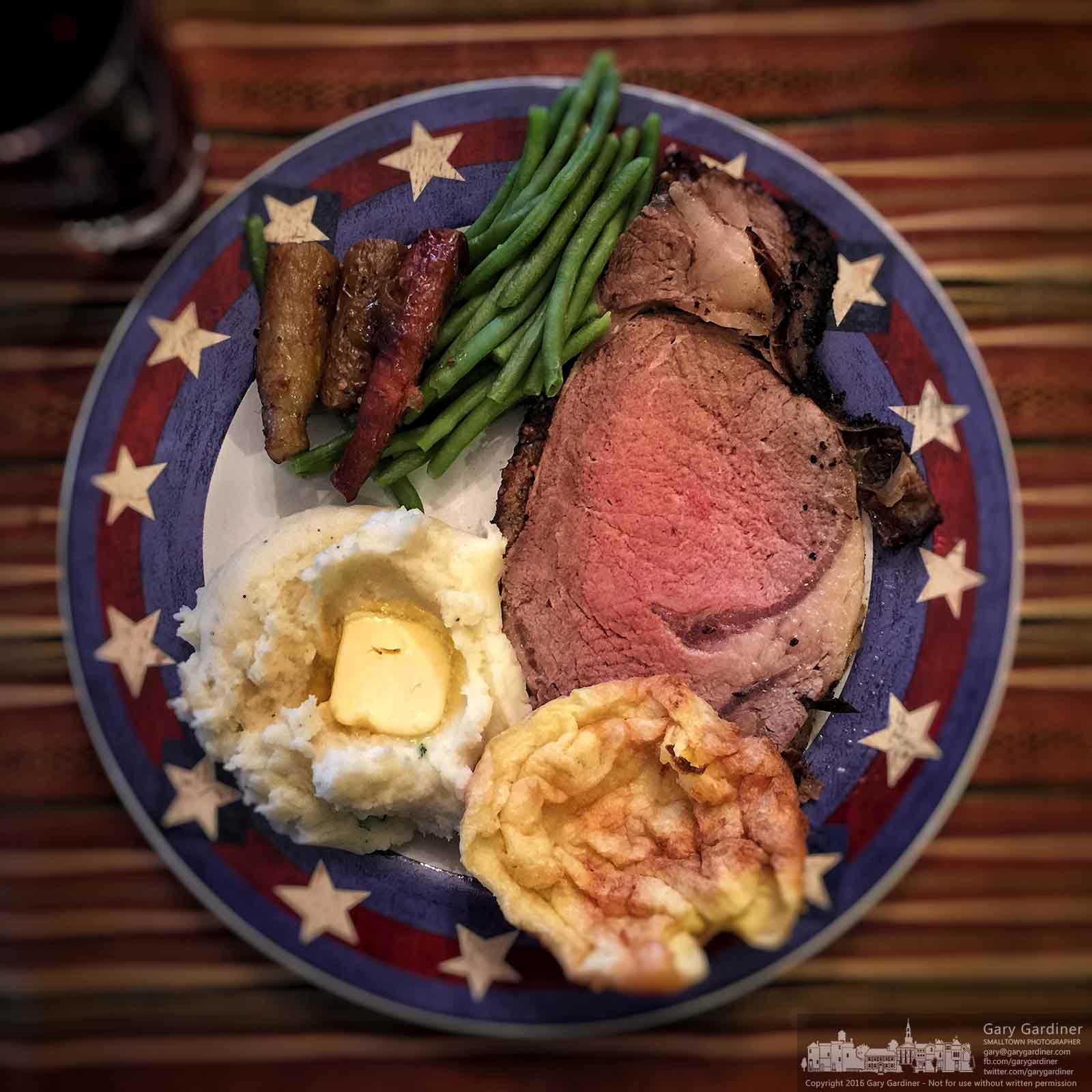 A Christmas dinner plate displaying prime rib, garlic mashed potatoes, green beans, roasted carrots, and Yorkshire pudding sits on the table ready for dining. My Final Photo for Dec. 25, 2016.