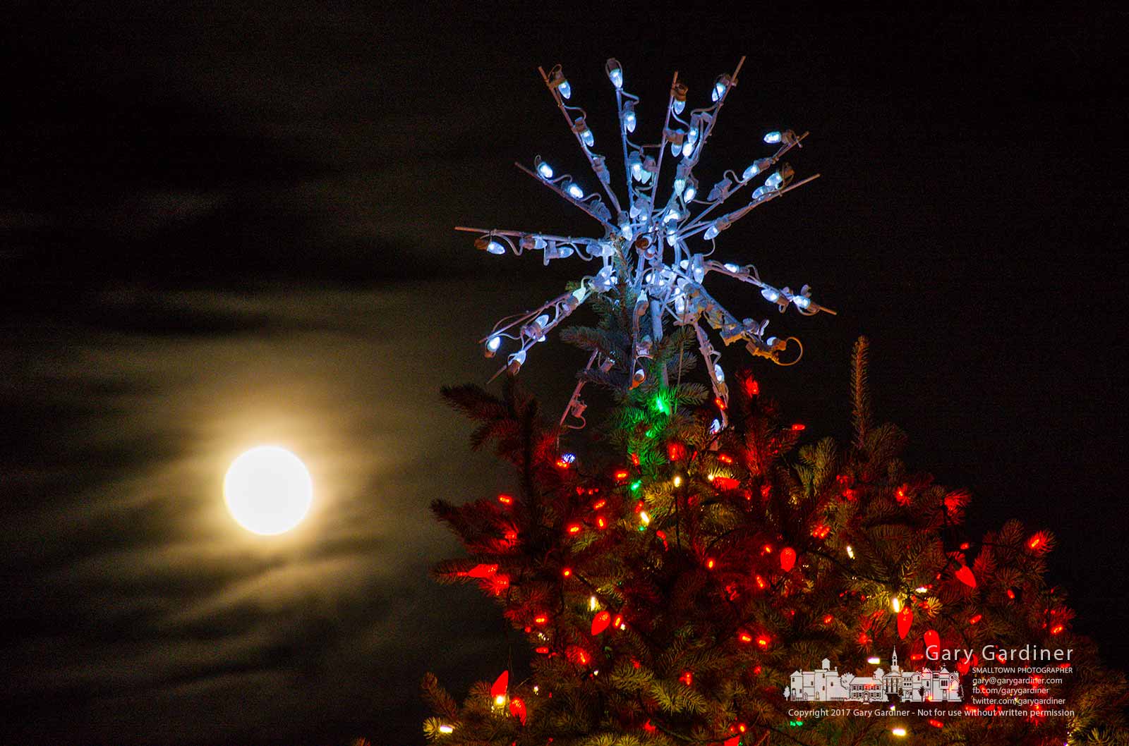 The near full moon slightly obscured by a cloud bank rises behind the star atop the holiday tree in the courtyard at city hall. My Final Photo for Dec. 2, 2017.