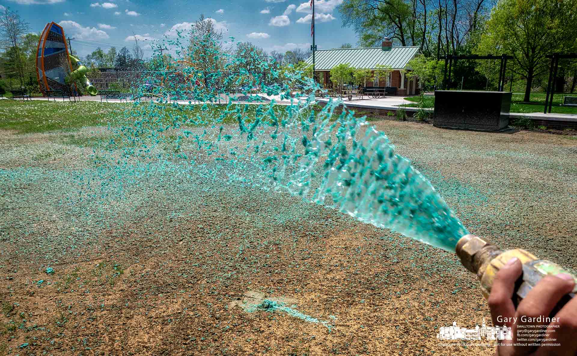 A landscaper sprays a mixture of water, grass seed, and a green mulch onto sections of Hanby Park as it nears completion of the installation of a new playground and water spray area. My Final Photo for May 8, 2018.