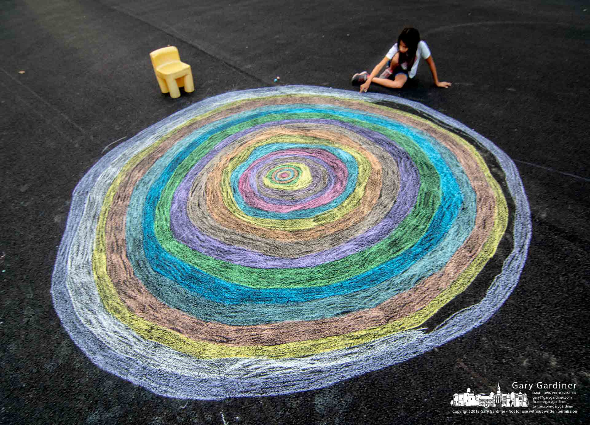 A young girl completes another circle drawn in chalk as she and her family begin coloring in with chalk the full cul-de-sac in front of their home. My Final Photo for July 6, 2018.