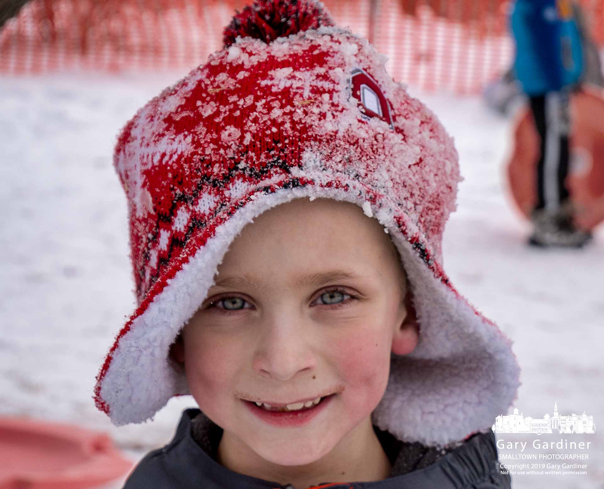 A young boy, stocking cap coated with snow and his cheeks turned red in the cold, smiles after ascending the sledding hill at Alum Creek Park North following another successful run down the slope. My Final Photo for Feb. 1, 2019.