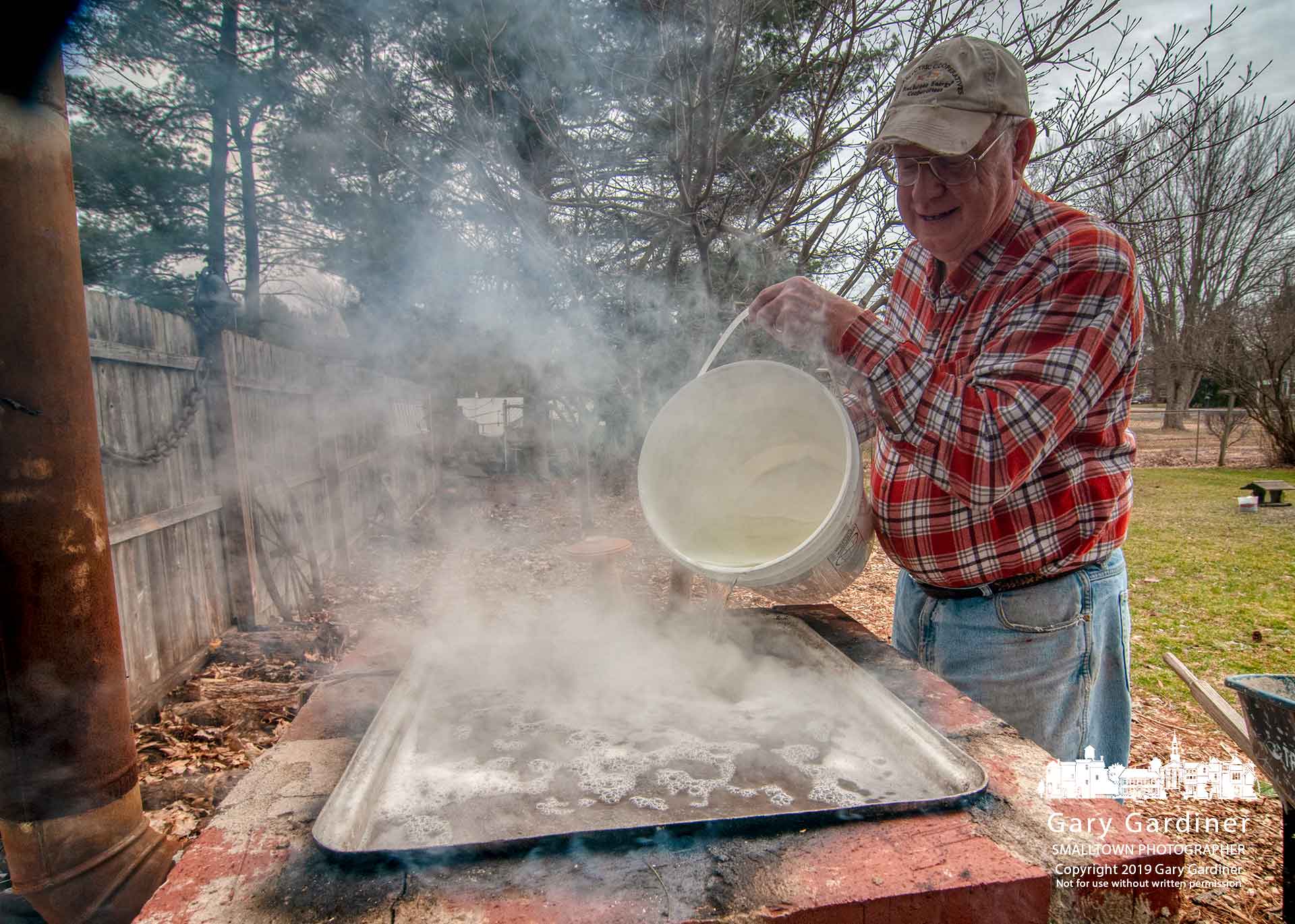 Bernie Woller pours fresh sugar maple sap into his wood-fired brick and concrete block evaporator where he will end up with more than six gallons of maple syrup from 250-plus gallons of sap collected from the trees in his yard. My Final Photo for March 13, 2019.