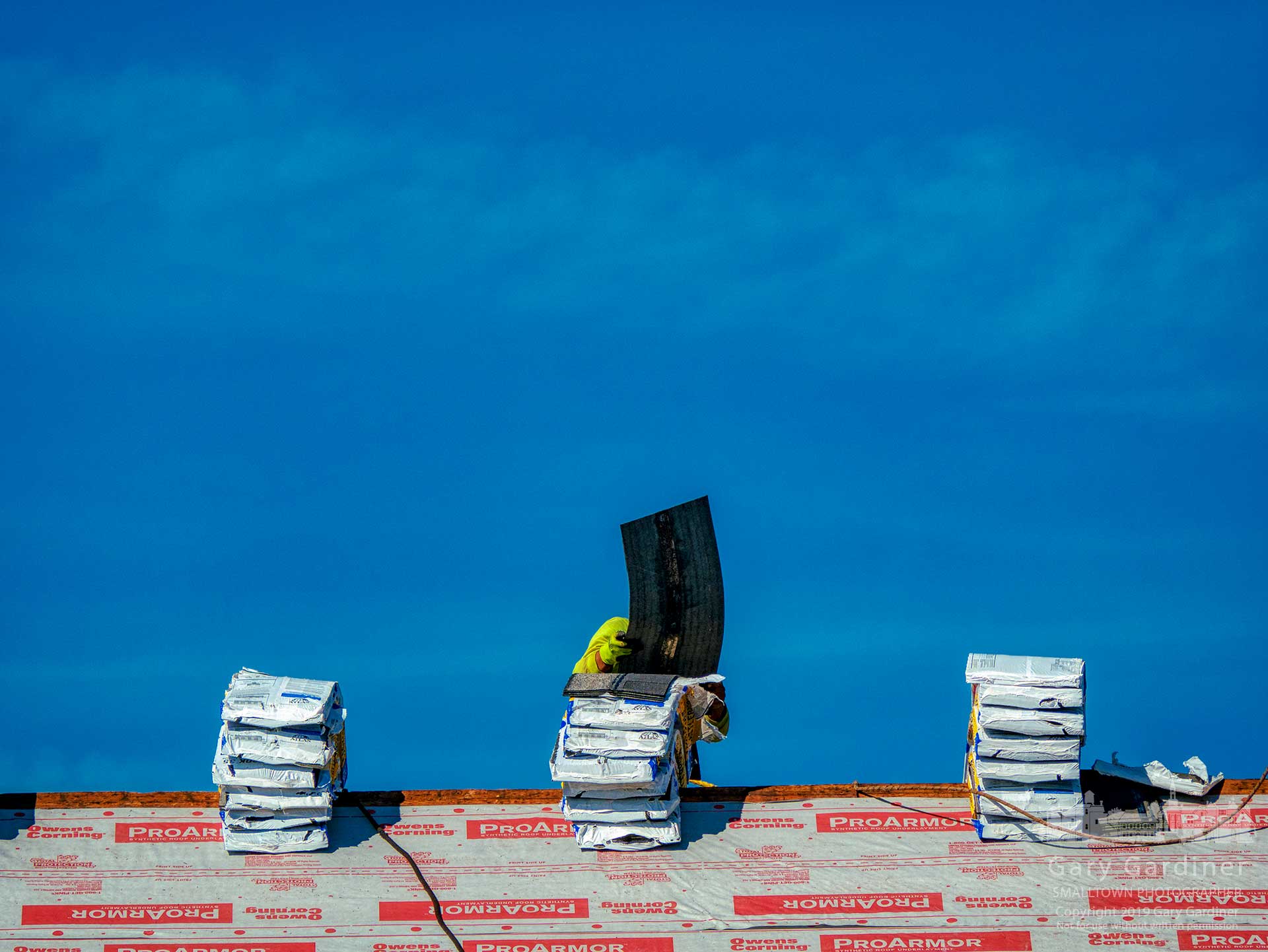A roofer tosses a shingle from its bundle sitting on the peak of a roof being reshingled on South State Street. My Final Photo for April 3, 2019.