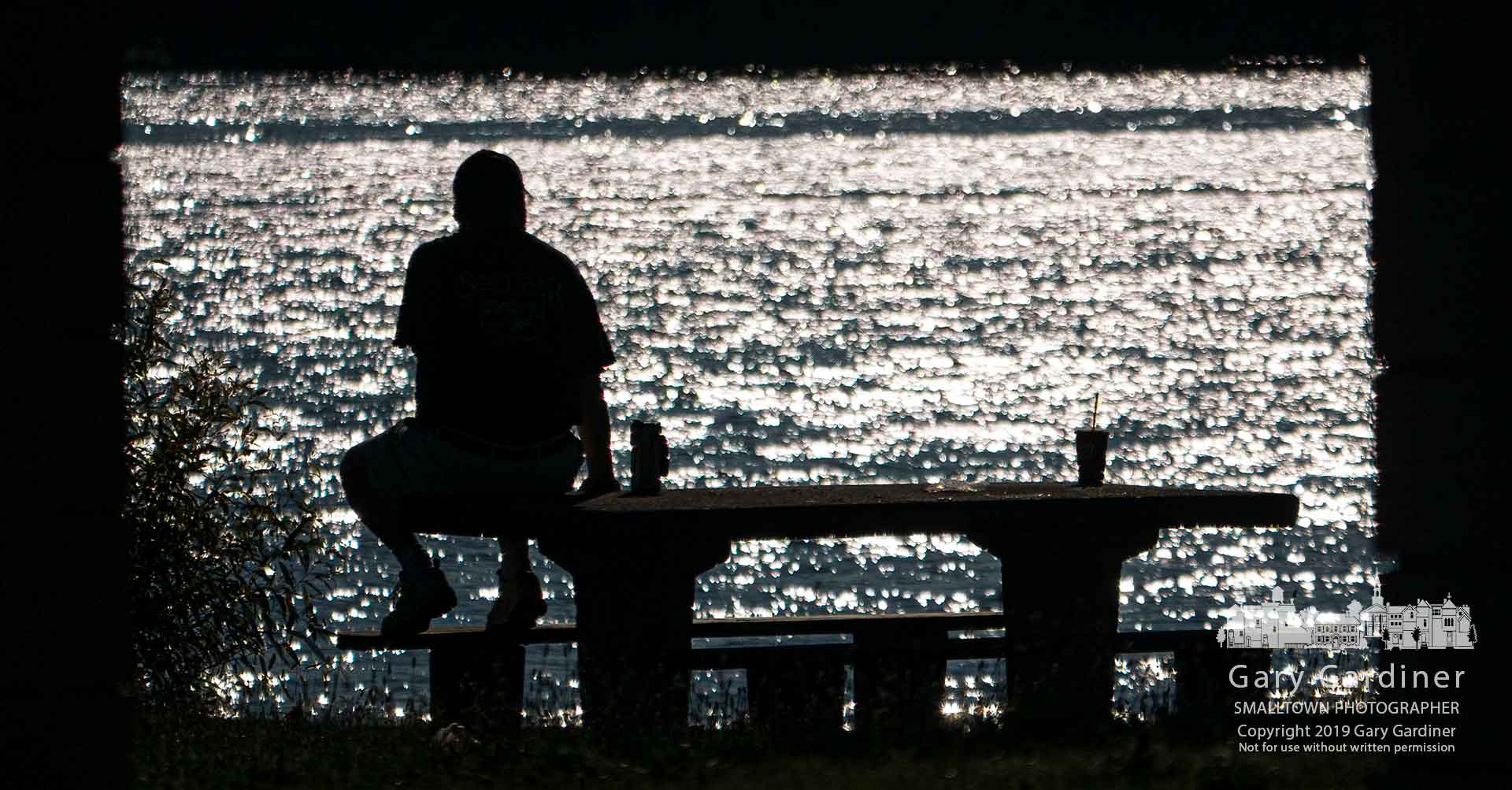 A man bathed in light from the morning sun reflecting off Hoover Reservoir sits on a picnic table at Red Bank Park. My Final Photo for July 23, 2019.