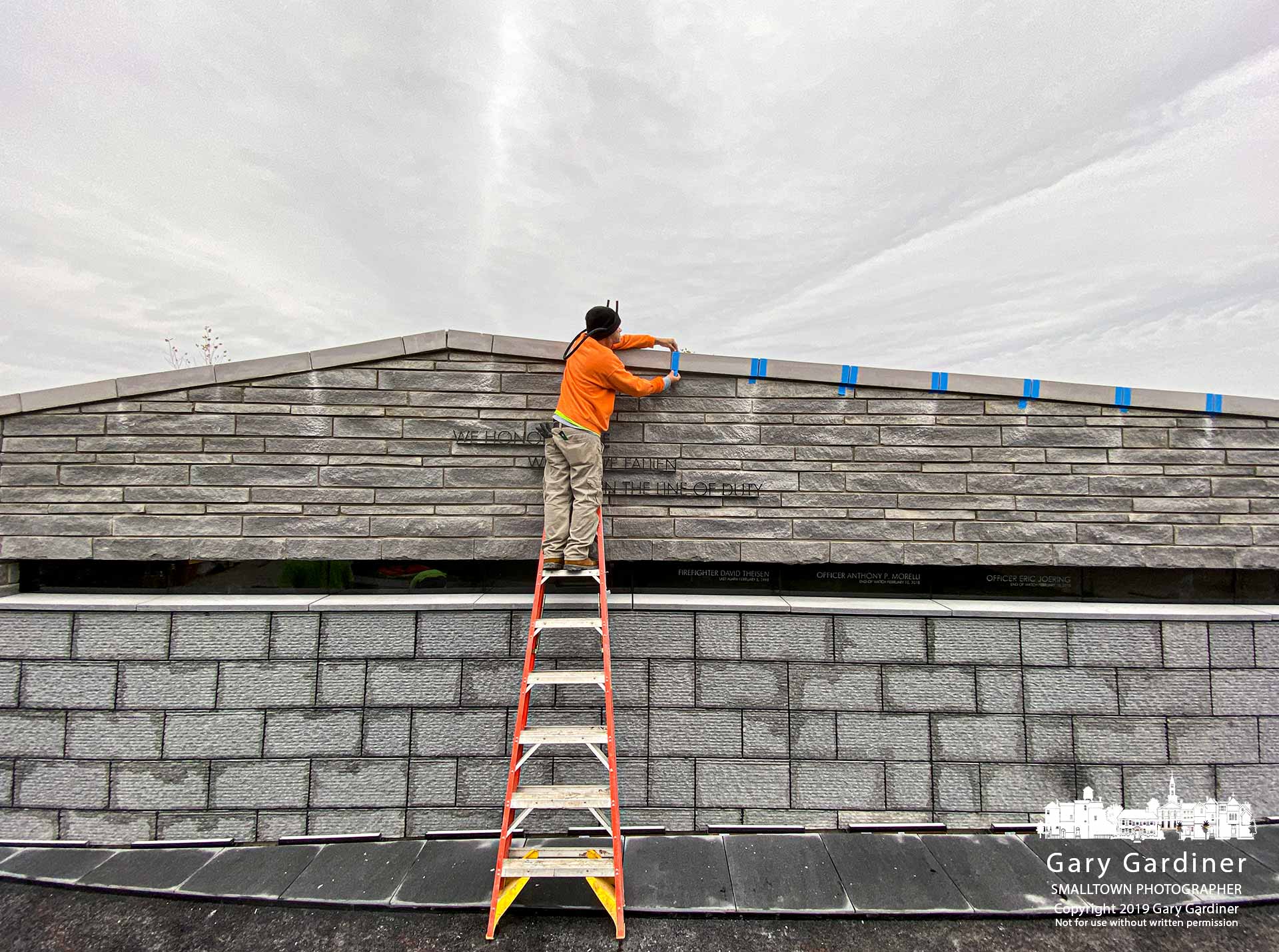A construction worker places protective tape on seams between sections of the new fountain wall in First Responders Park before sealing them as the park nears completion. My Final Photo for Oct. 25, 2019.