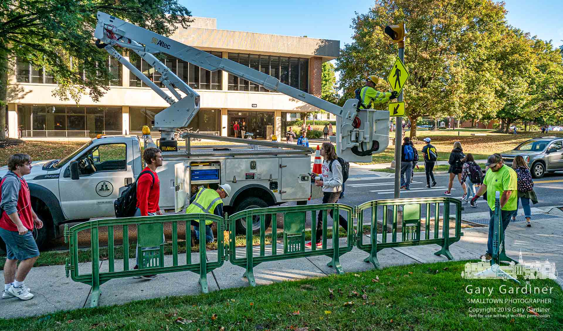 Otterbein students navigate their way past Westerville city workers placing barriers on the sidewalk and new flashing lights at the crosswalk on West Main Street as part of the preparations for the Democratic candidate's debate. My Final Photo for Oct. 10, 2019.