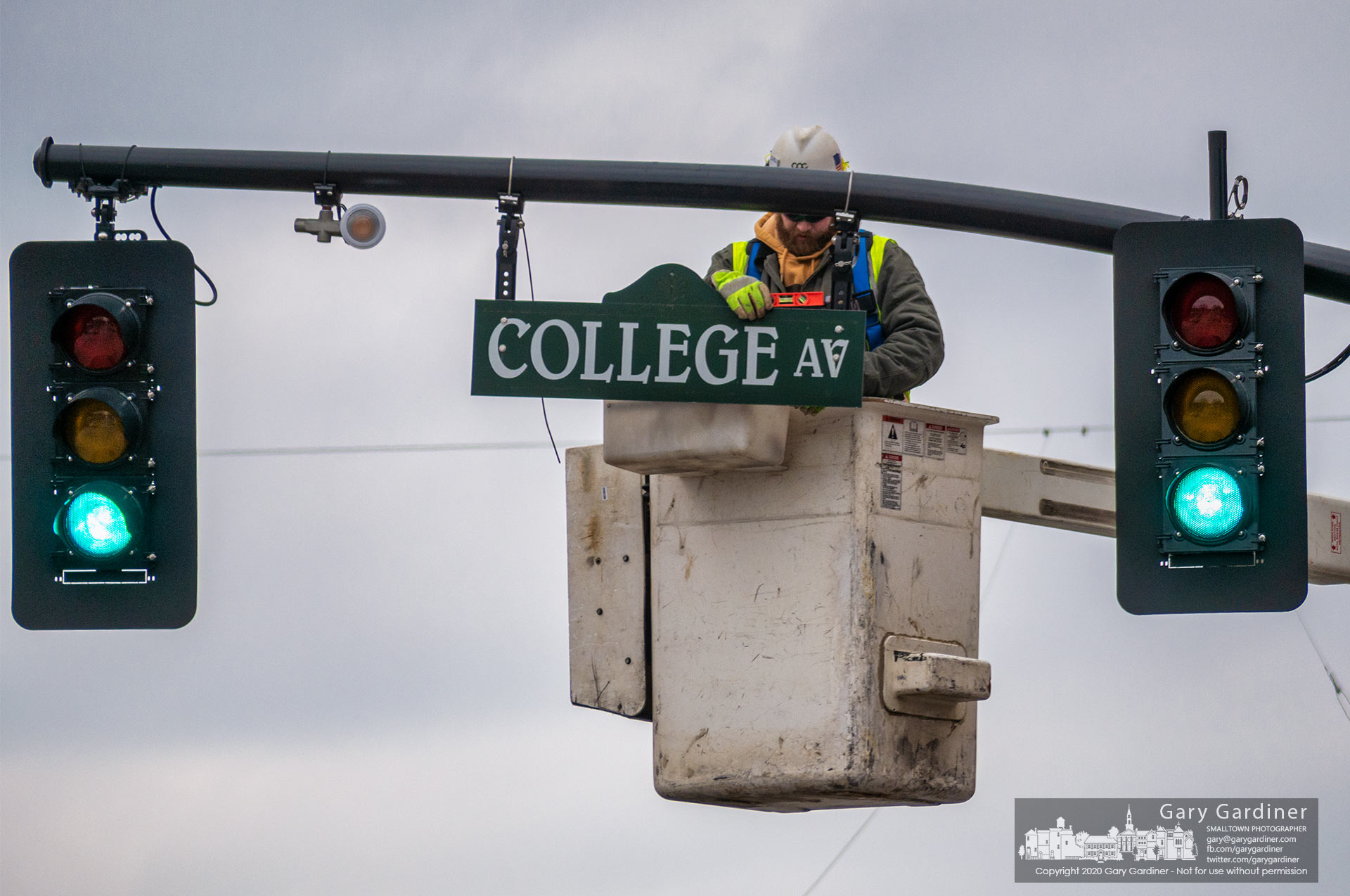 A worker levels the College Ave. street sign after rehanging it as a swinging sign from its previous fixed position on the traffic signal arm. My Final Photo for Jan. 20, 2021.