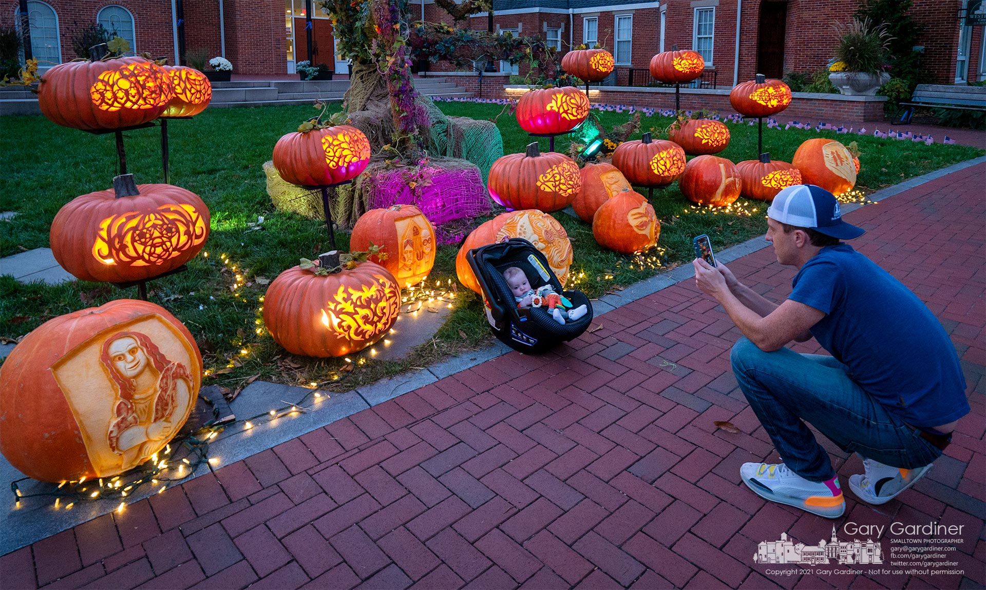 A father photographs his infant child settled into a carrier in front of the Pumpkin Glow display at Westerville City Hall. My Final Photo for Oct. 20, 2021.