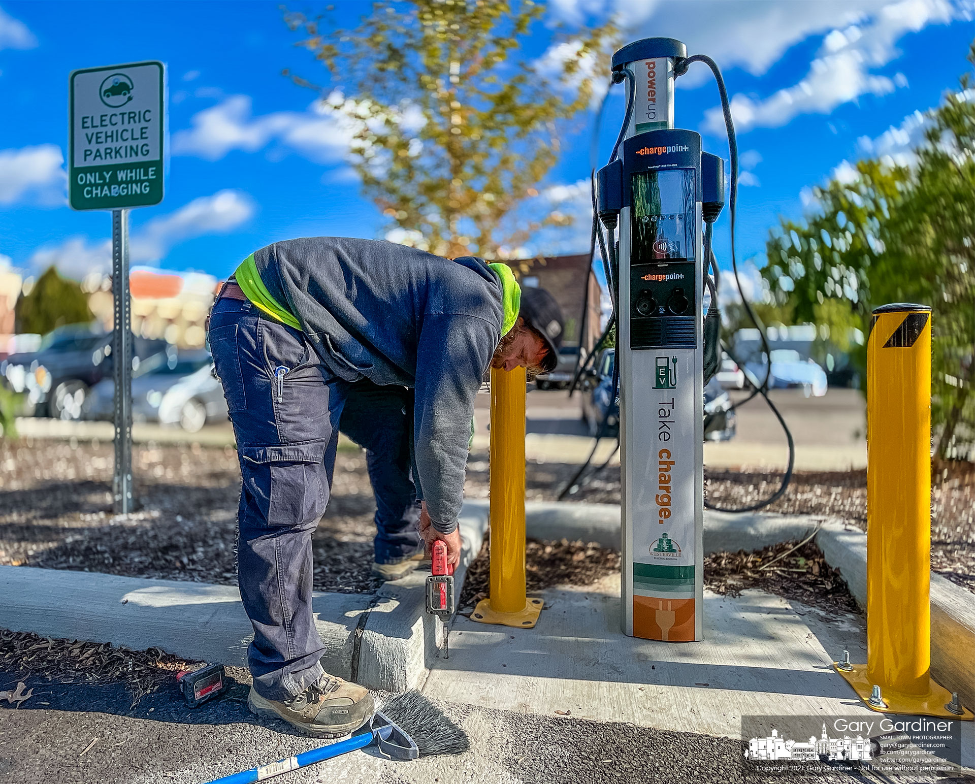 A technician installs a bollard to guard damage to one of the two new electric vehicle charging stations installed in the new parking lot behind city hall. My Final Photo for Nov. 2, 2021.