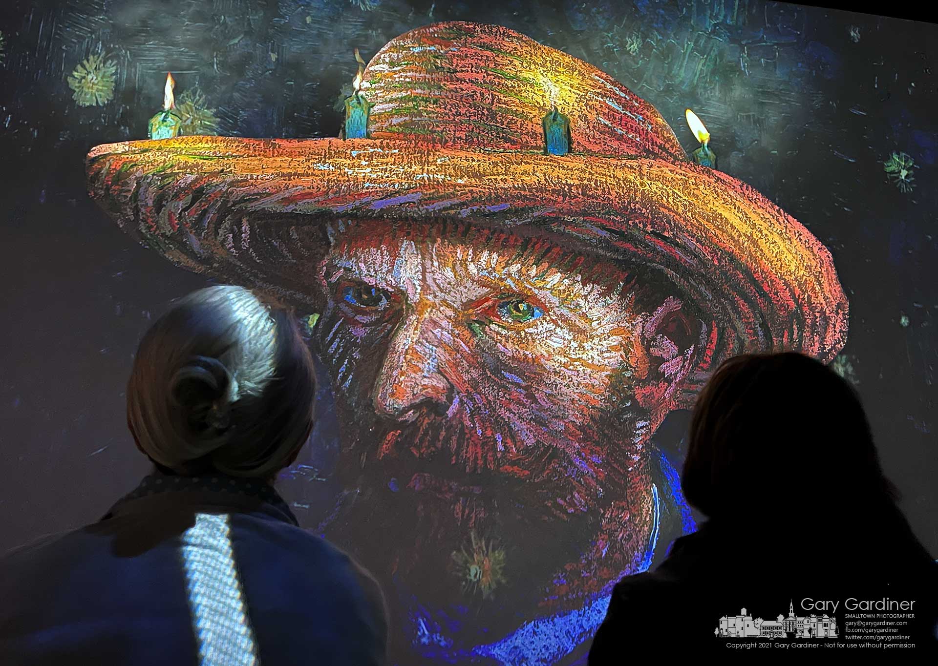 Two women study a portrait of Vincent Van Gogh during the Immersive Van Gogh multimedia show in a closed furniture store converted into a modern digital museum. My Final Photo for Nov. 9, 2021.