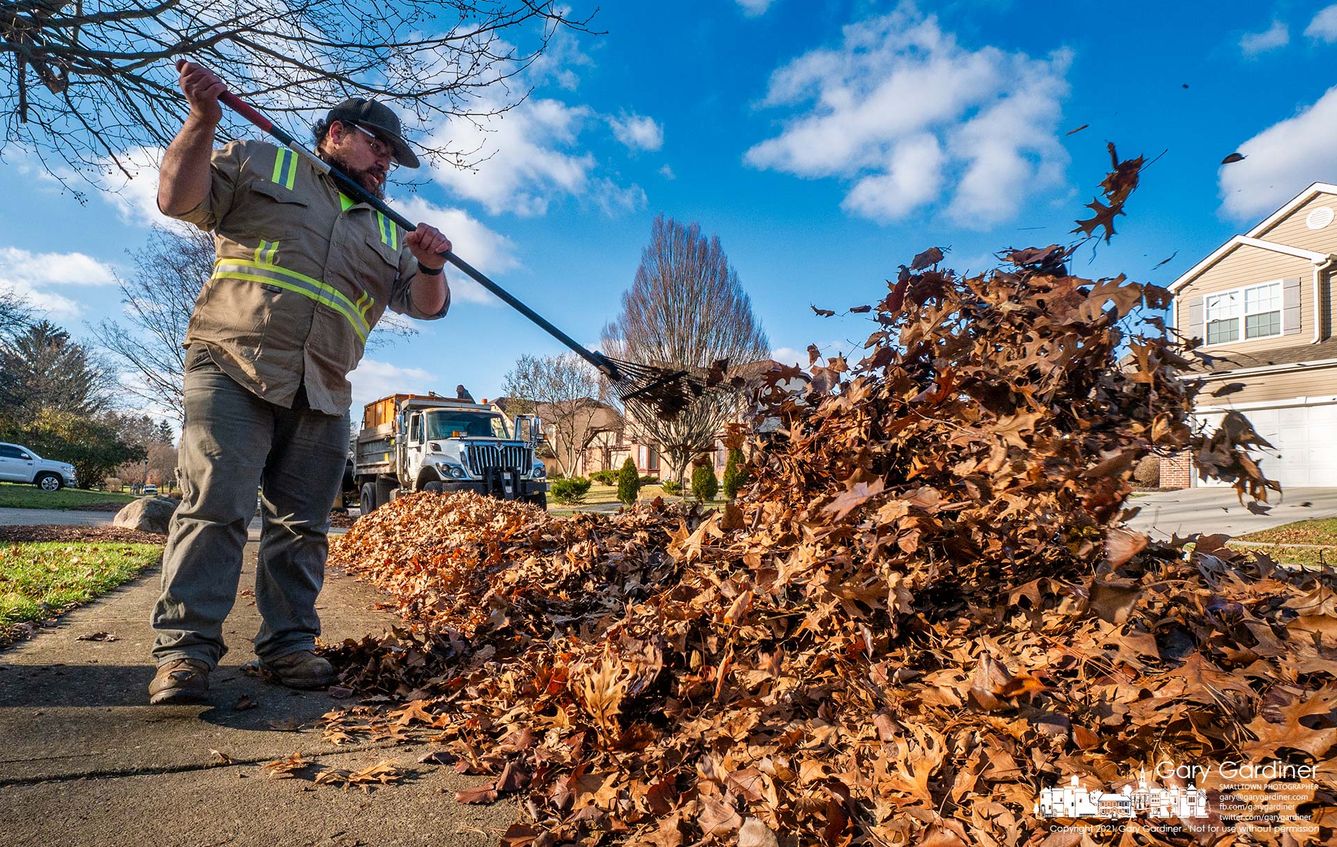 A city worker uses a rake to throw stacks of leaves to the curb so they can be vacuumed away as the city's final weeks of leaf disposal come to an end. My Final Photo for Dec. 22, 2021.