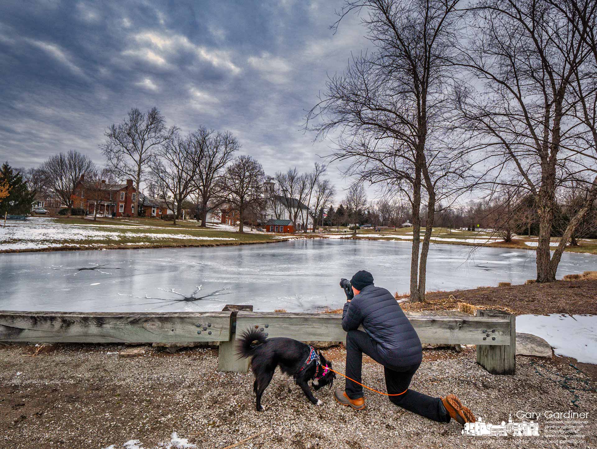A photographer kneels for a better perspective on the frozen pond that accentuates the old farm buildings at Heritage Park in Westerville. My Final Photo for Jan. 22, 2022.