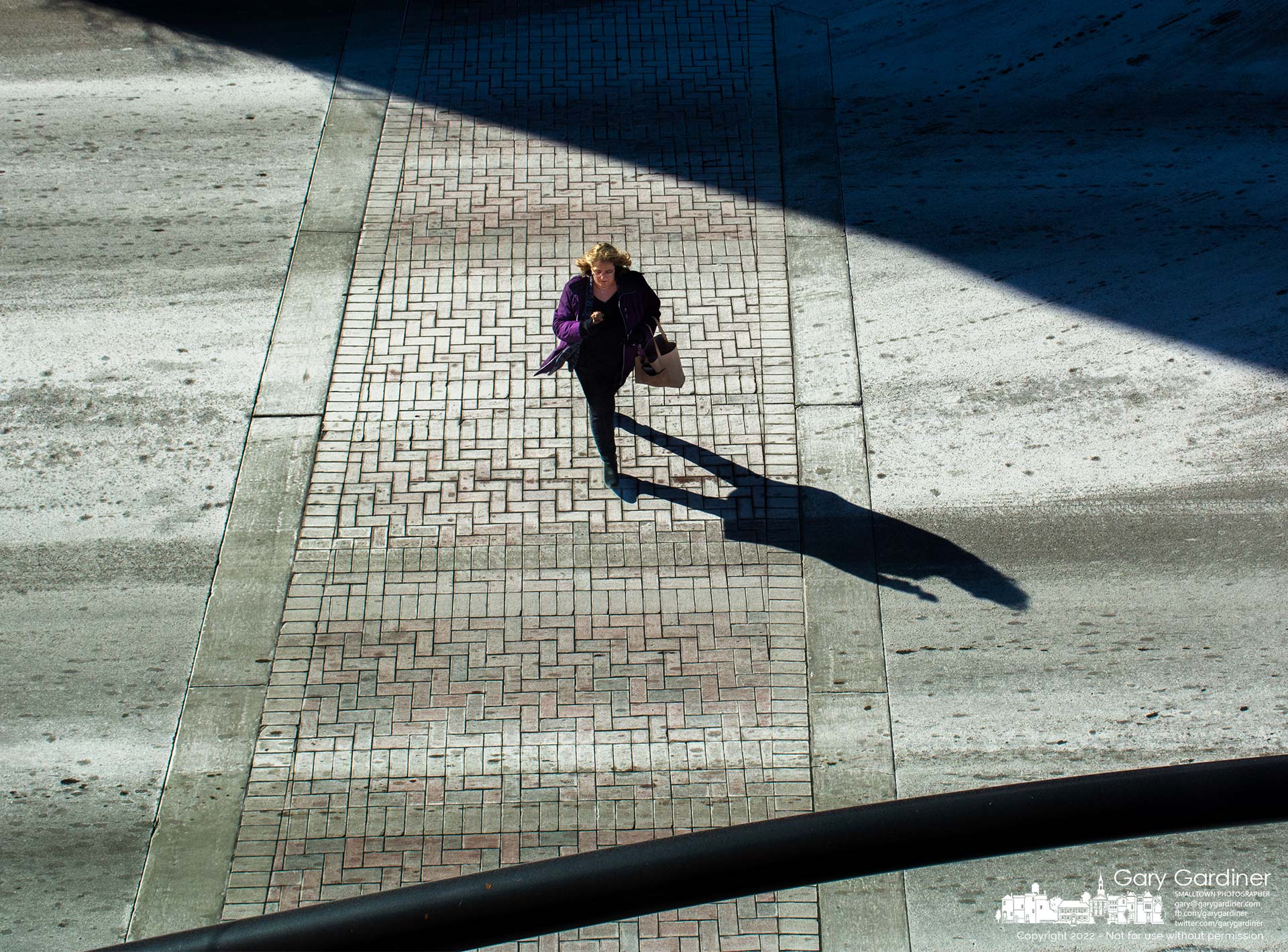 A woman crosses State Street where the red-brick walkway wears a dusty coating of brine sprayed by the city to help melt any snow and ice that maybe happen at the intersection with Main Street. My Final Photo for Jan/. 21, 2022.
