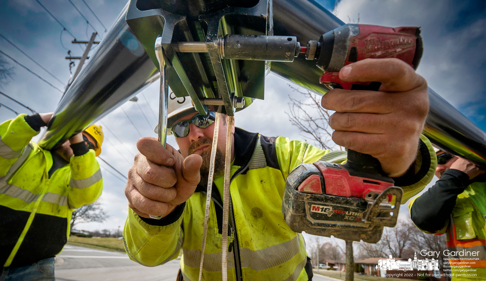 A workman tightens bolts that fasten arms holding new led streetlights in the median on Huber Village Boulevard replacing the old lights. My Final Photo for March 10, 2022.