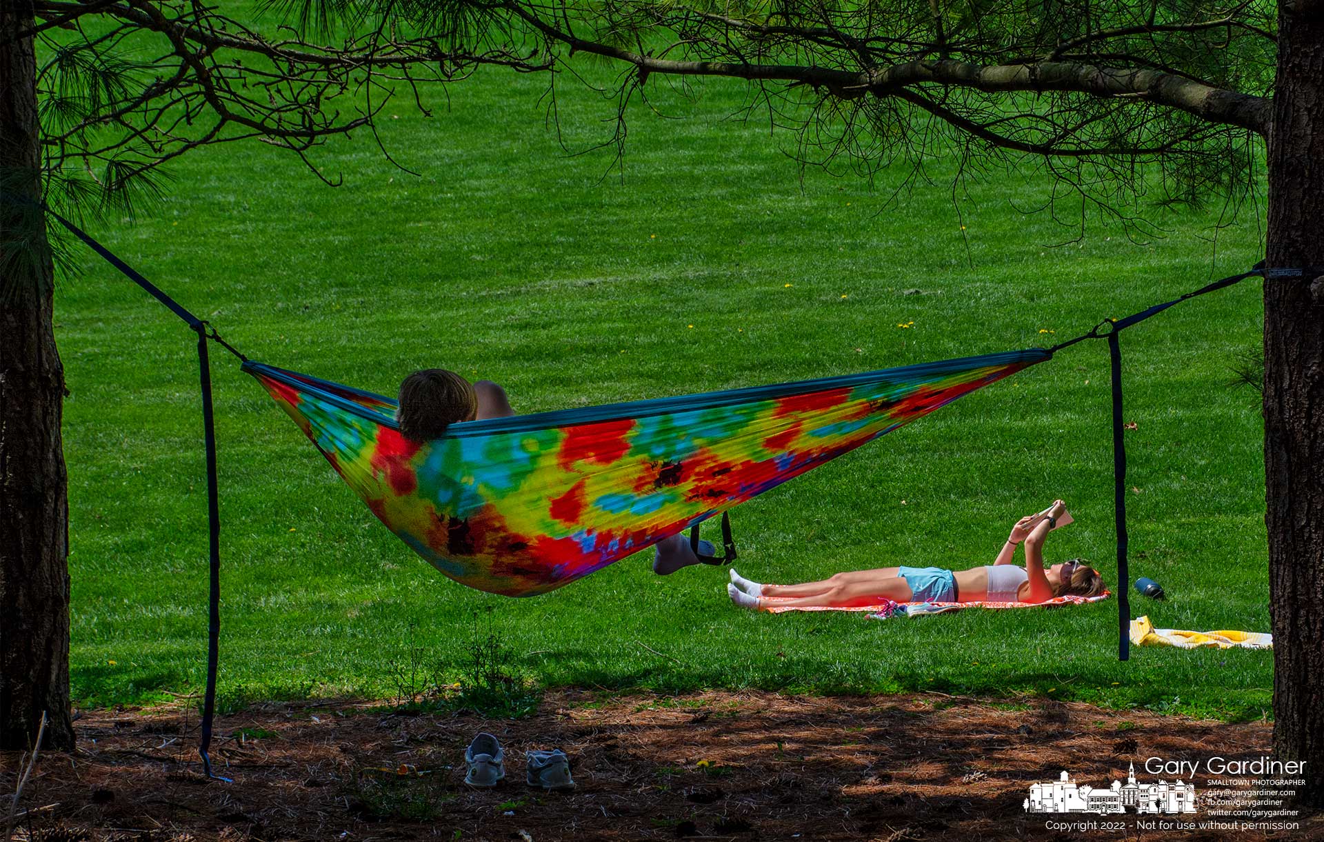 Two young people pick different locations to enjoy the warmest day of Spring with one resting in a shaded hammock as the other reads her book in the warm glow of the sun. My Final Photo for April 23, 2022.