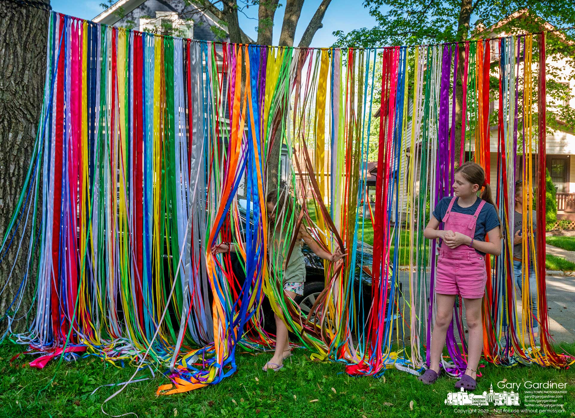 A young girl runs through a curtain of colored ribbons hanging between trees at the Vine Street Art Walk in Uptown Westerville Sunday evening. My Final Photo for May 15, 2022.