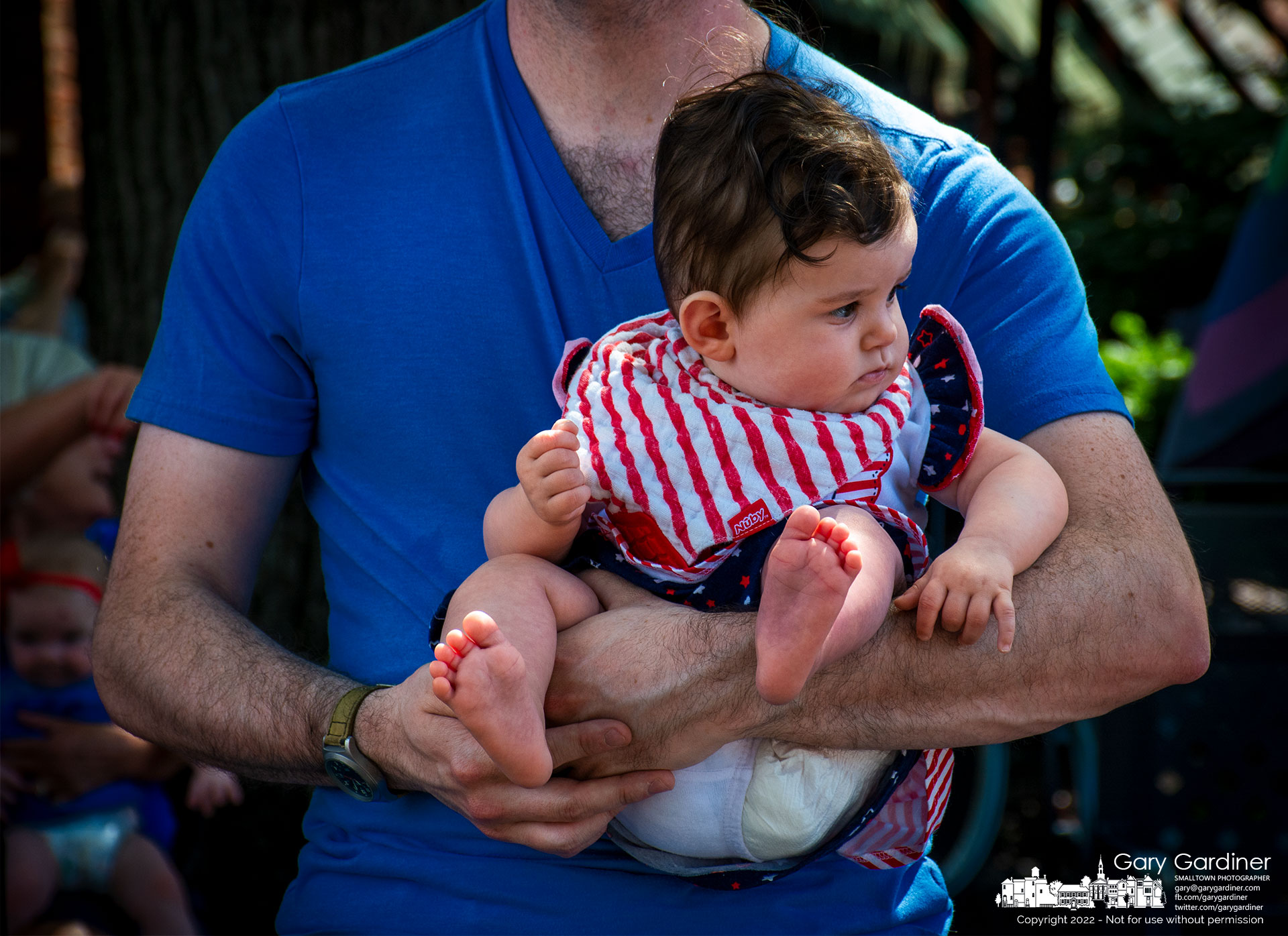 A father's arms cradle his child as they watch her first Fourth of July parade. My Final Photo for July 4, 2022.