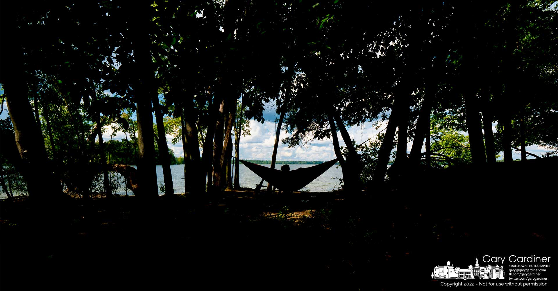 A couple rests in their hammock hanging from trees in the shade along the treeline at the northern shore of Oxbow boat ramp on Hoover Reservoir. My Final Photo for August 17, 2022.