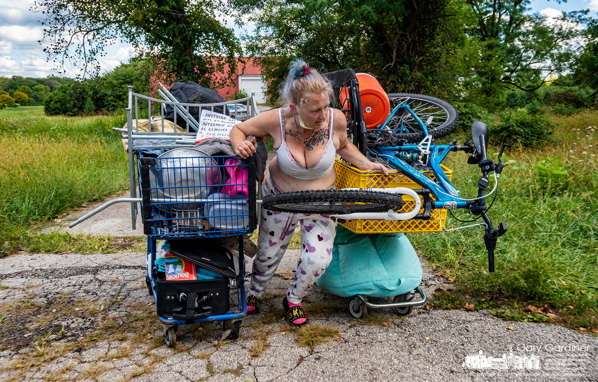 A homeless woman pushes two carts of her belongings out of the driveway at the Braun Farm as she and her husband leave the property after staying in the barn for a week. My Final Photo for Sept. 12, 2022.