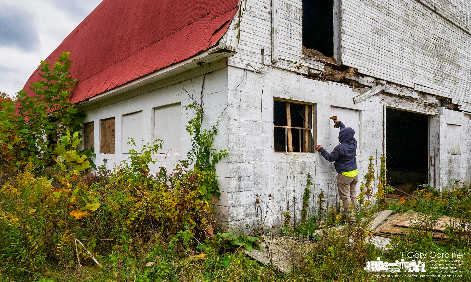A worker removes plywood covering windows at the barn on the Braun Farm in preparation for removing lead paint and asbestos from the barn and abandoned farmhouse as both are prepared for demolition. My Final Photo for October 18, 2022.