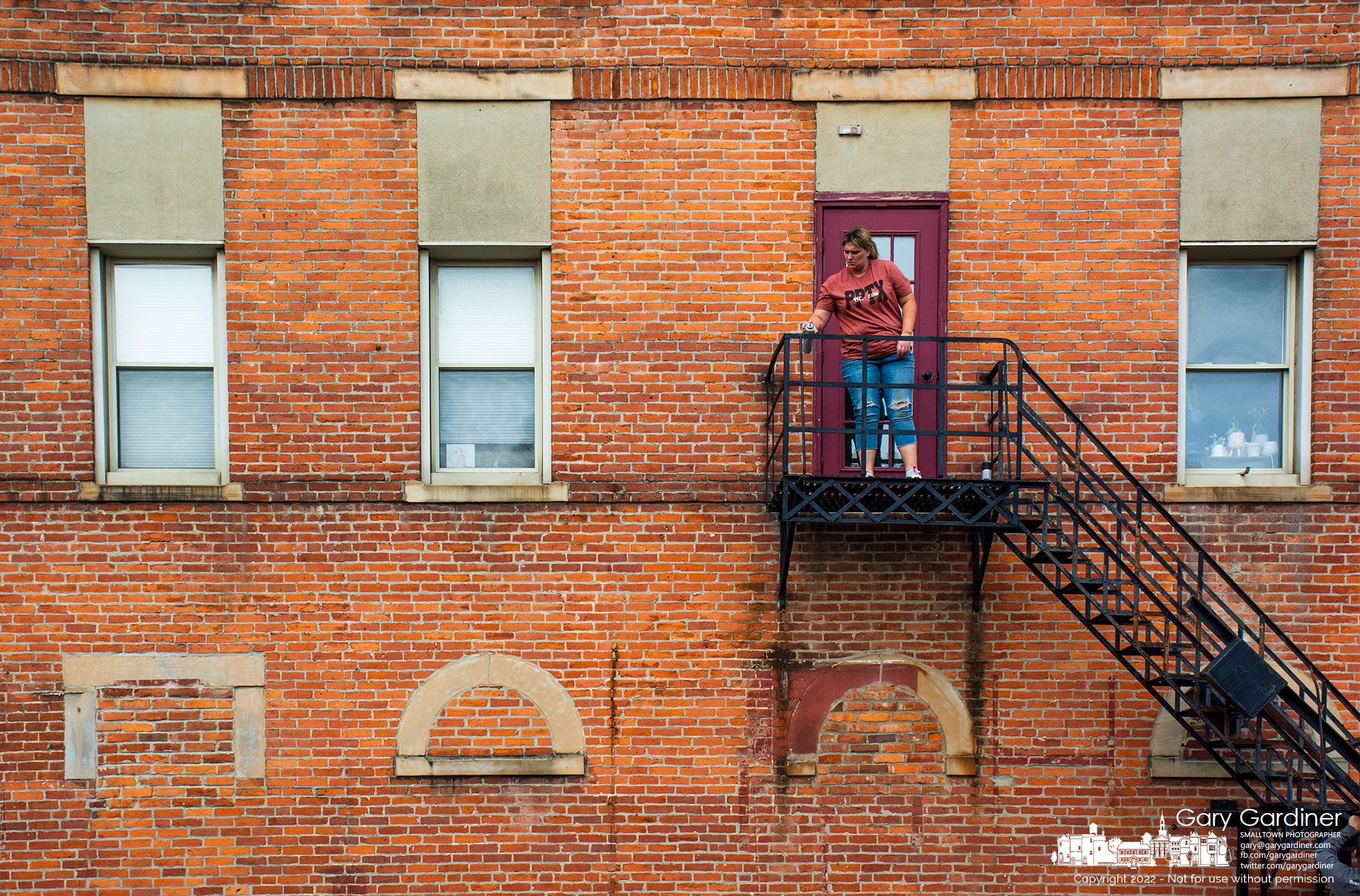 A woman spray paints the fire escape landing for the apartments above Graeter's Ice Cream after scraping away rust form the structure. My Final Photo for October 25, 2022.