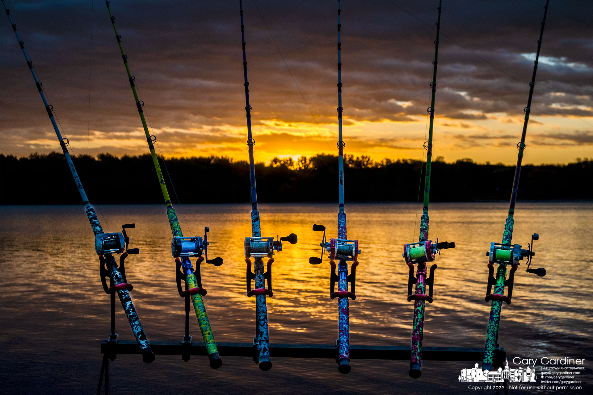 Six colorful rods and reels used by three fishermen sit in a homemade holding rack as their owners stand nearby and wait in the old, breezy morning at sunrise over Hoover Reservoir. My Final Photo for October 15, 2022,