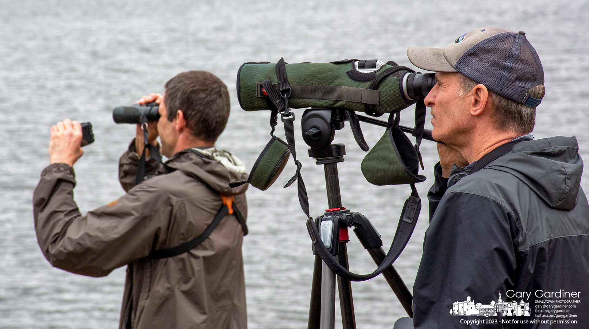 A pair of birders, one holding binoculars in one hand and a camera in the other, scan Hoover Reservoir for a Pacific Loon to add a checkmark to their annual list of birds they've watched. My Final Photo for January 3, 2023.