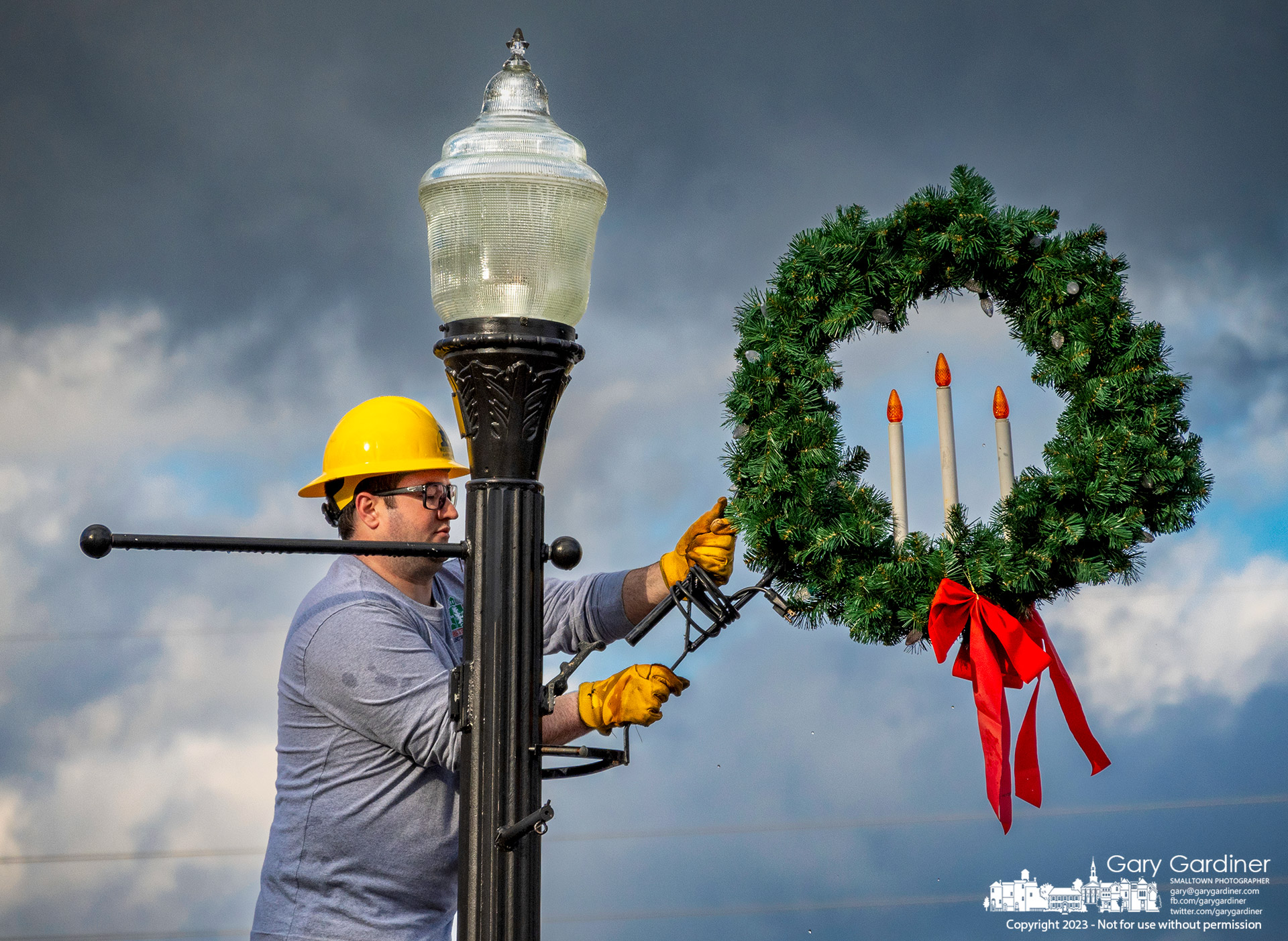 A city worker removes a Christmas wreath attached to a light pole near the library as the year-end holiday celebration comes to an end with the removal of the lights. My Final Photo for January 4, 2023.