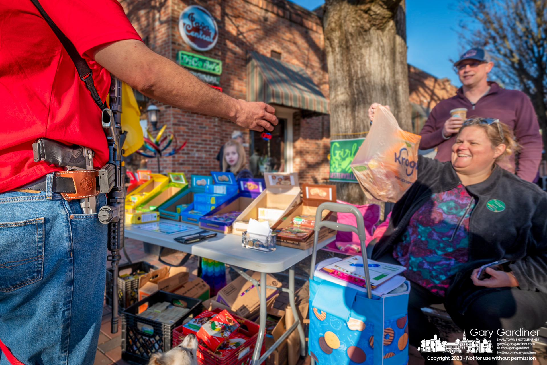 A gun-rights advocate carrying a semi-automatic rifle and pistol buys Girl Scout cookies from a stand set up at the brick walk beside Java Central in Uptown Westerville. My Final Photo for February 25, 2023.