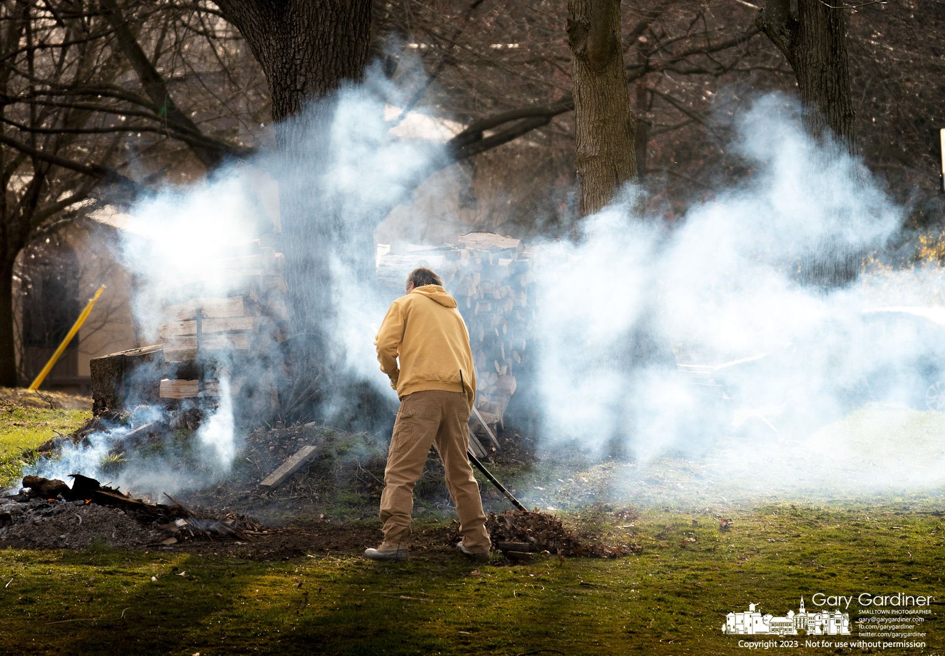 A man rakes leaves and debris from a fallen tree into a burning pile in the backyard of his home that borders Hoover Reservoir. My final Photo for March 21, 2023.