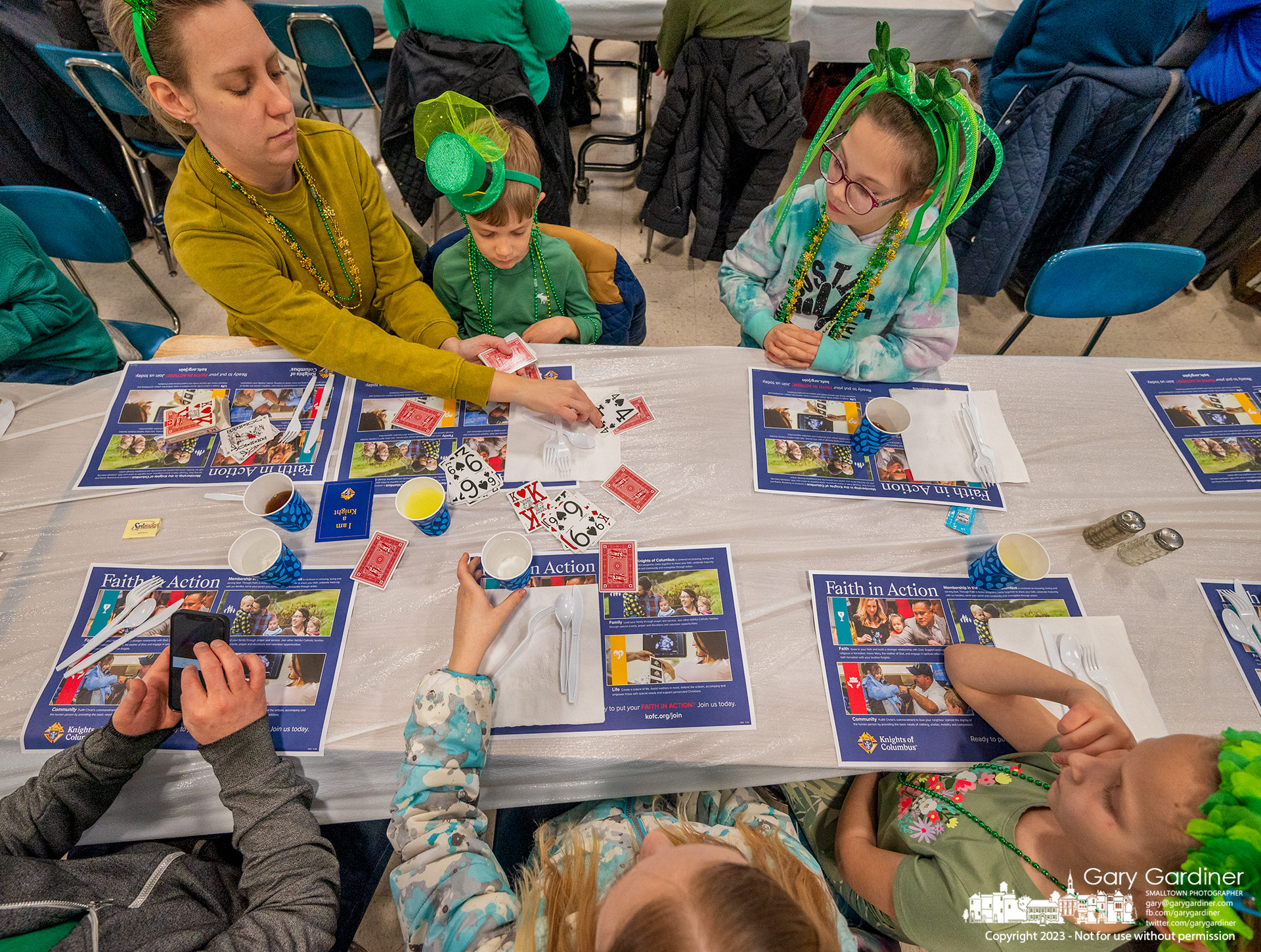 A family wearing St. Patrick green plays a card game after ordering their fish meal at the St. Paul the Apostle Catholic Church's Lenten Friday fish fry. My Final Photo for March 17, 2023.