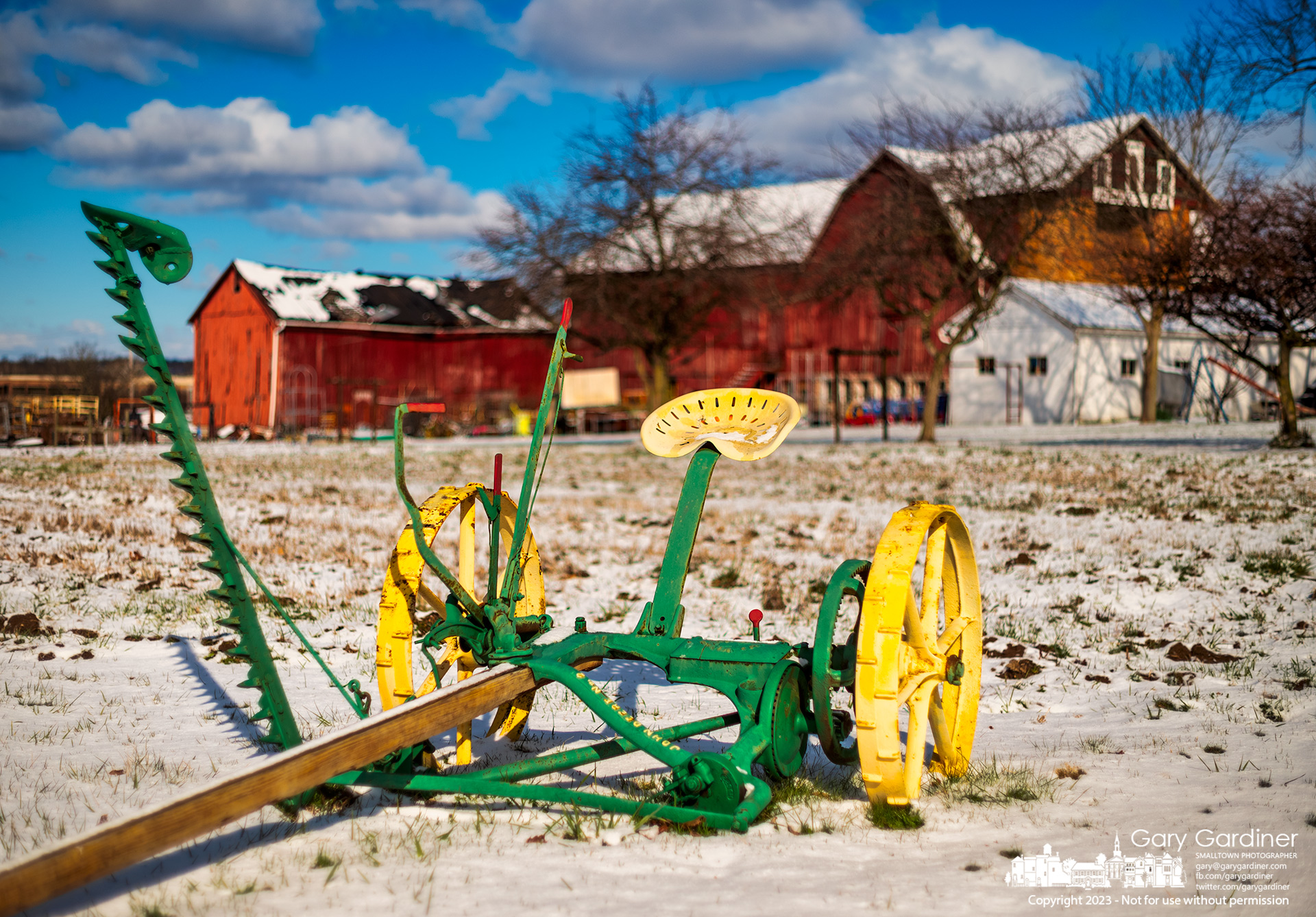 The morning sun casts a bright sharp light over an antique sickle mower sitting at the edge of a snowy garden and field at the Yarnell Farm on Africa road. My Final Photo for March 14, 2023.