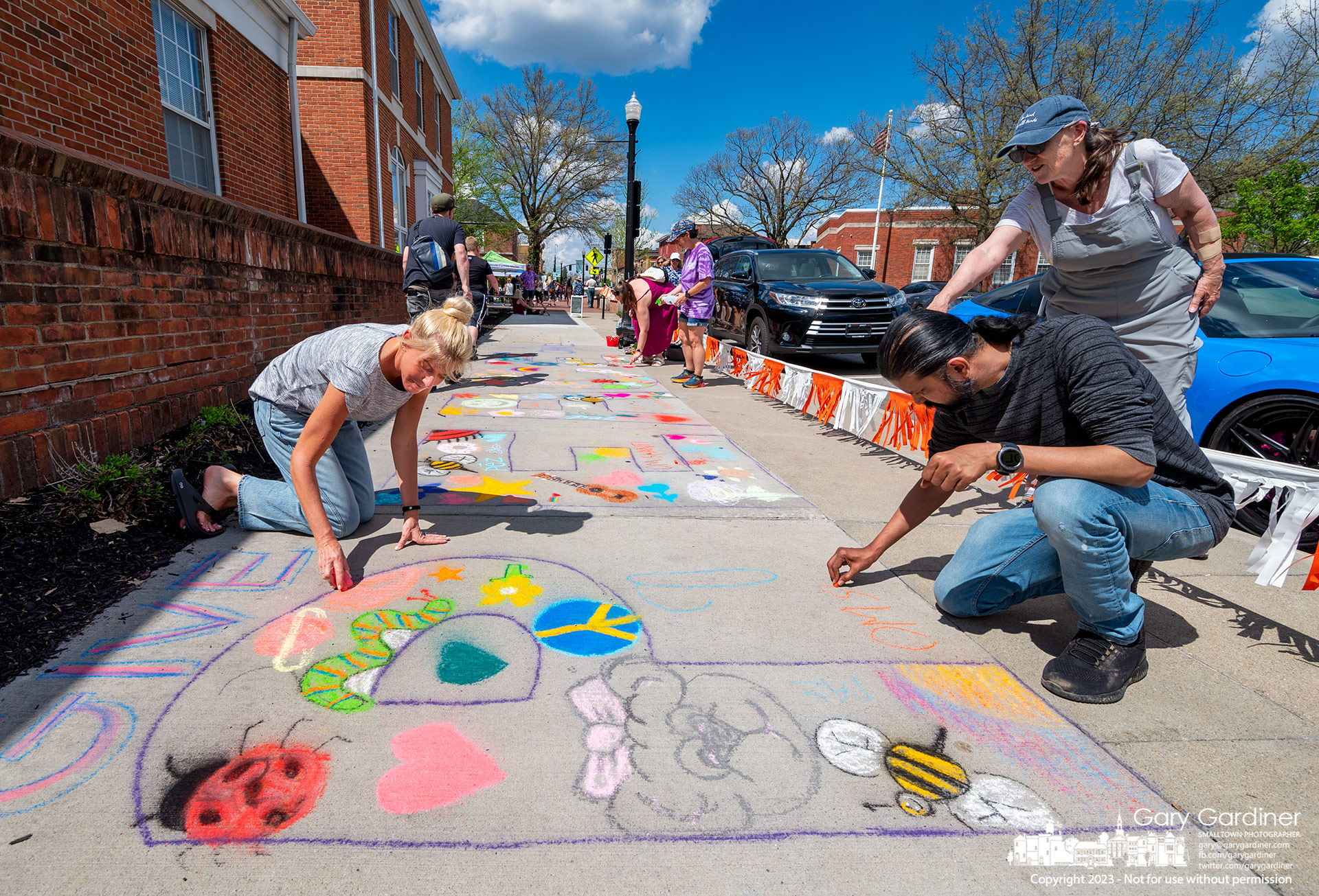 Amateur artists get instructions on completing a chalk mural proclaiming "Give Peace A Chance" on the sidewalk in front of city hall during the Art Hop in Uptown Westerville Saturday. My Final Photo for April 15, 2023.
