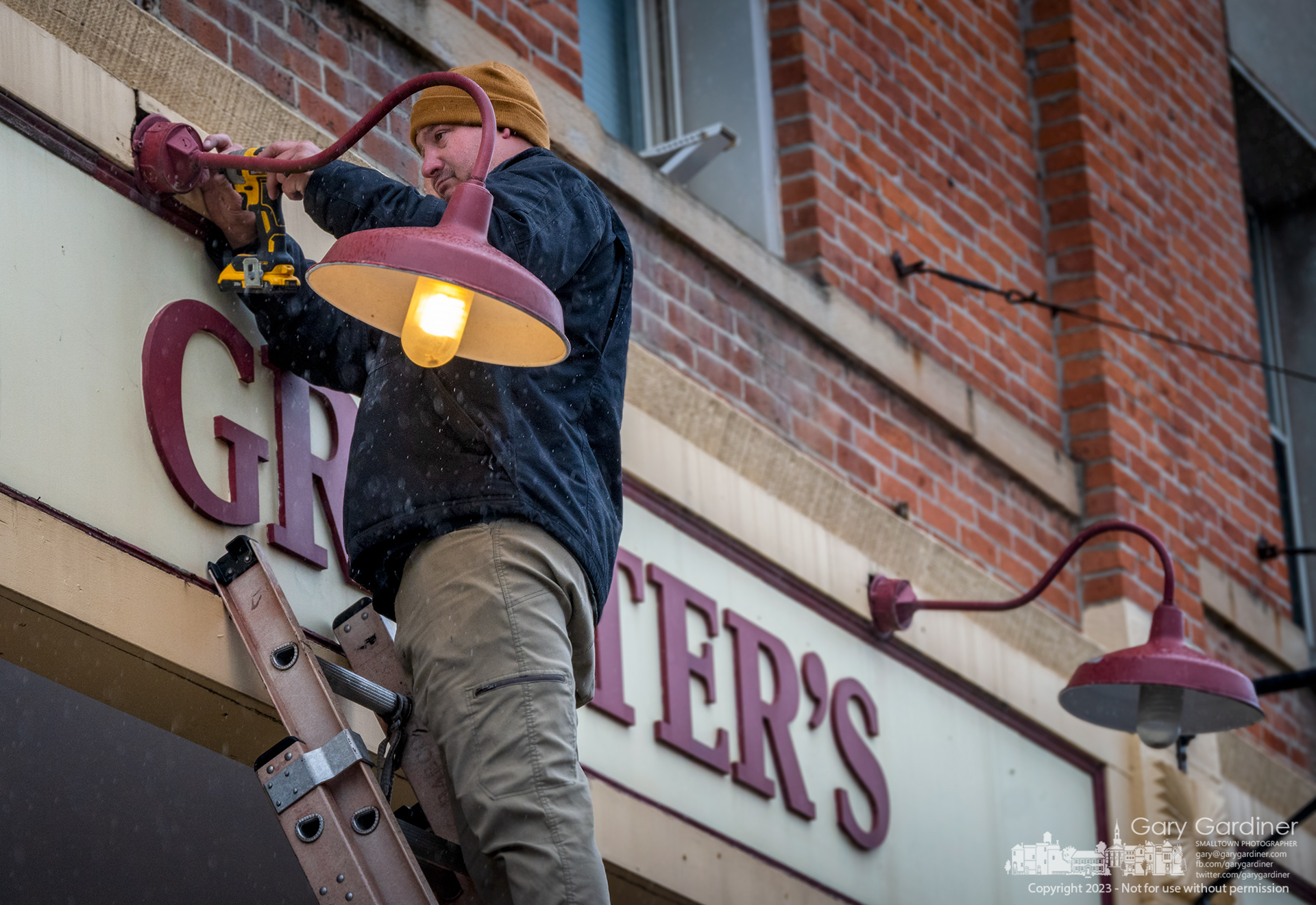 An electrician anchors a repaired light fixture to the Graeter's sign in front of the Uptown Westerville ice cream store. My Final Photo for May 2023.