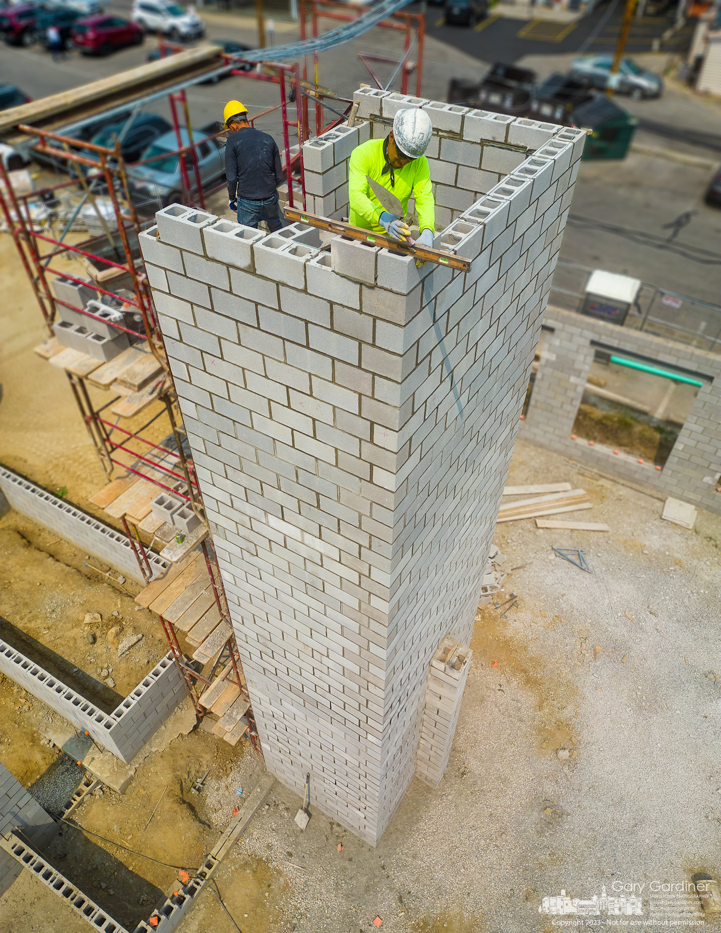 A block mason checks the level of a layer of concrete blocks built to house an elevator for a business and apartment building under construction on West College Ave. My Final Photo for June 7, 2023.