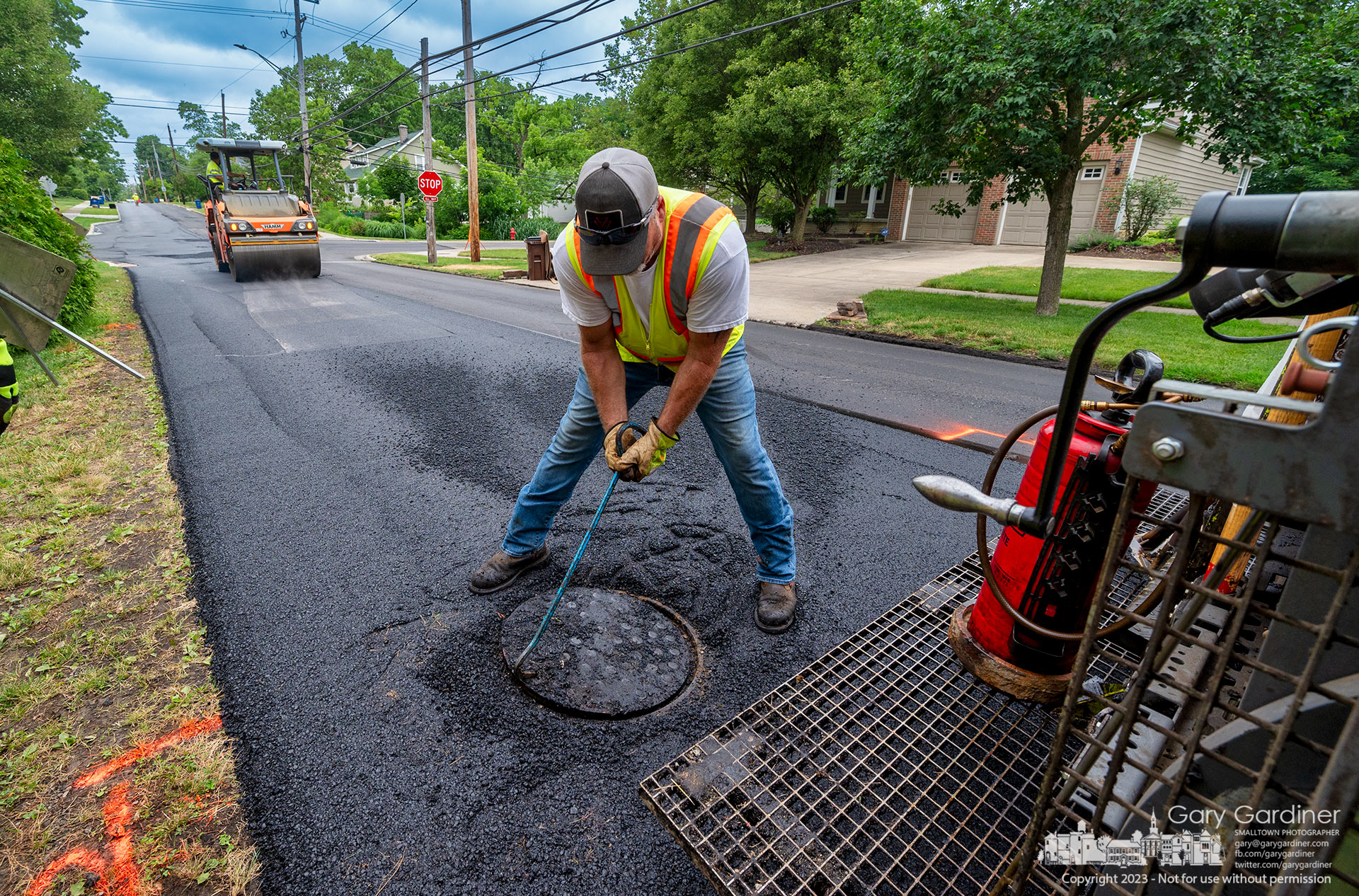 A worker settles a manhole cover into place after resetting its height following the application of a final layer of asphalt on East College just past Otterbein Avenue. My final Photo for June 20, 2023.