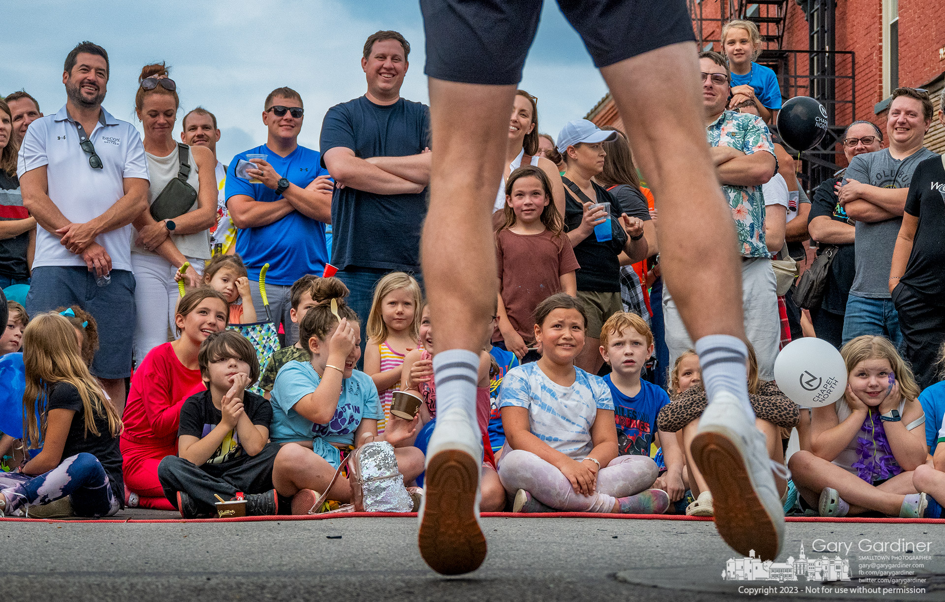 Adults and children react as a juggling contortionist passes an open-face tennis racket over his chest and shoulders warning them that he will have to dislocate his shoulder to accomplish the stunt during Fourth Friday in Uptown Westerville. My Final Photo for June 23, 2023.