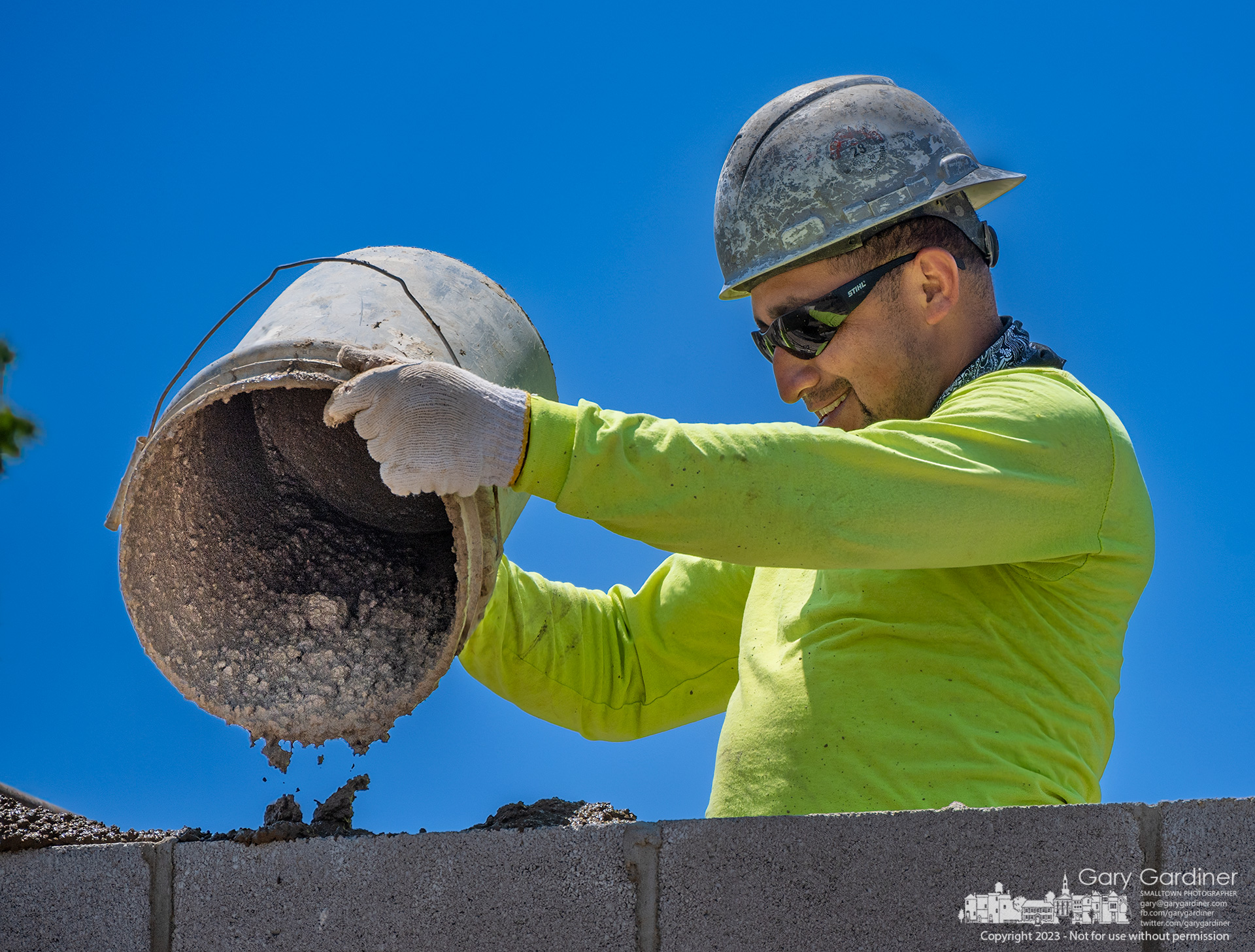 A mason pours a concrete mortar mix into the void of a section of the brick wall built for the first floor on a multi-story business and apartment building on West College in Uptown Westerville. My Final Photo for June 1, 2023.