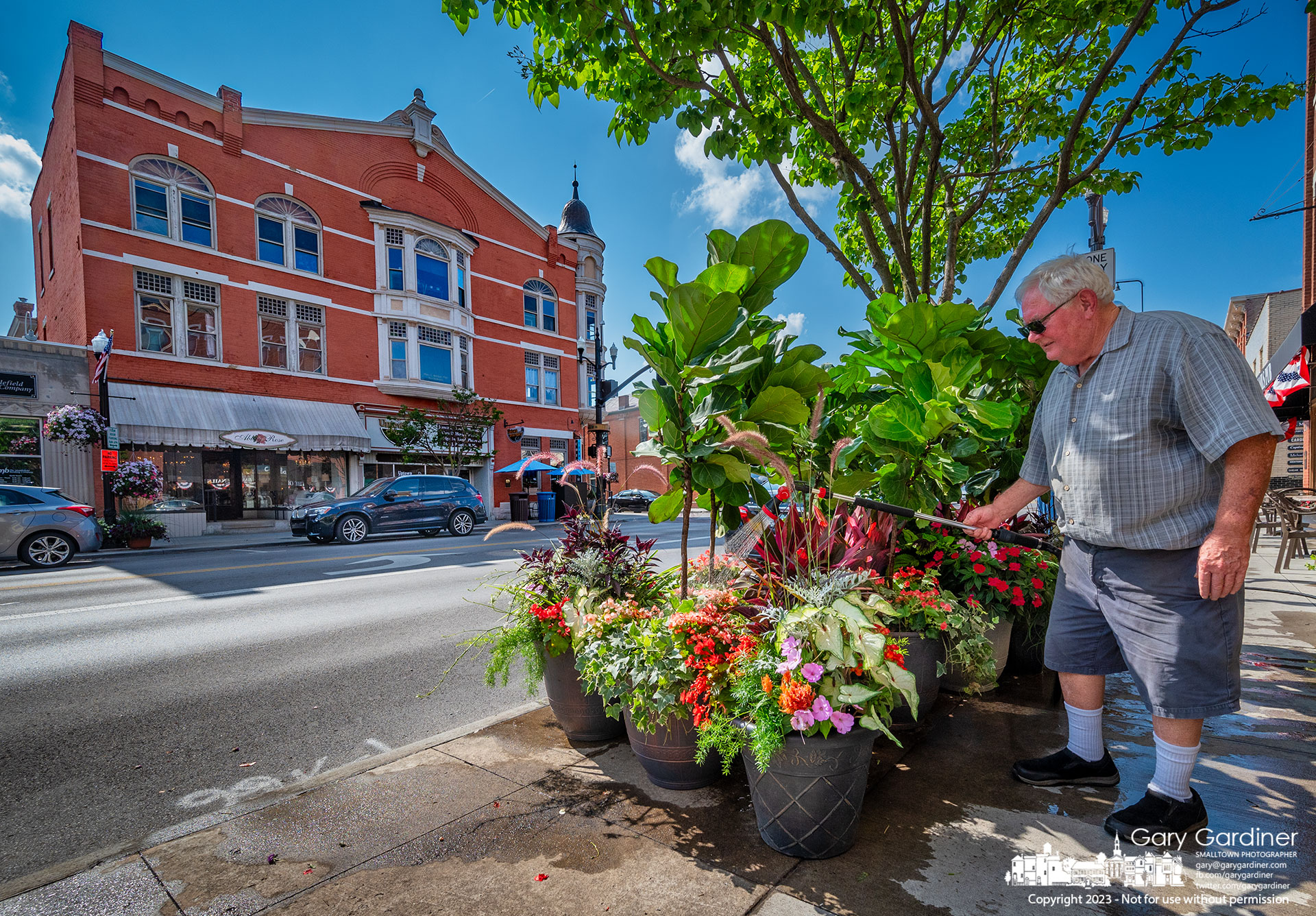 Florist Dave Talbott waters the plants and flowers he displays on the sidewalk in front of his Uptown Westerville shop creating a public garden maintained by him and his workers. My Final Photo for July 27, 2023.