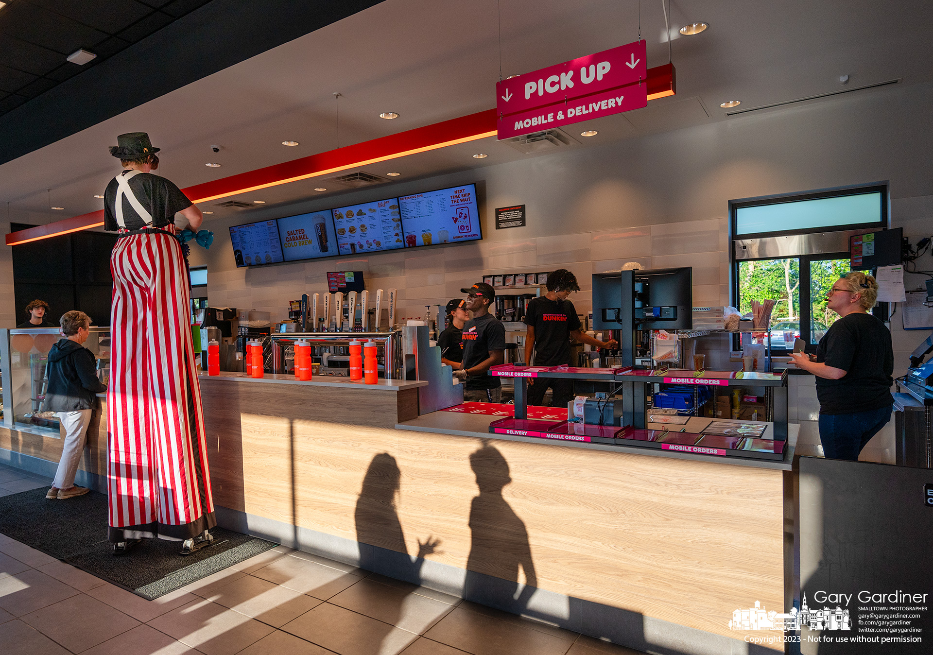 A stilted balloon animal artist orders coffee and donuts before ceremonies marking the grand opening of the Dunkin restaurant on South State Street. My Final Photo for July 11, 2023.