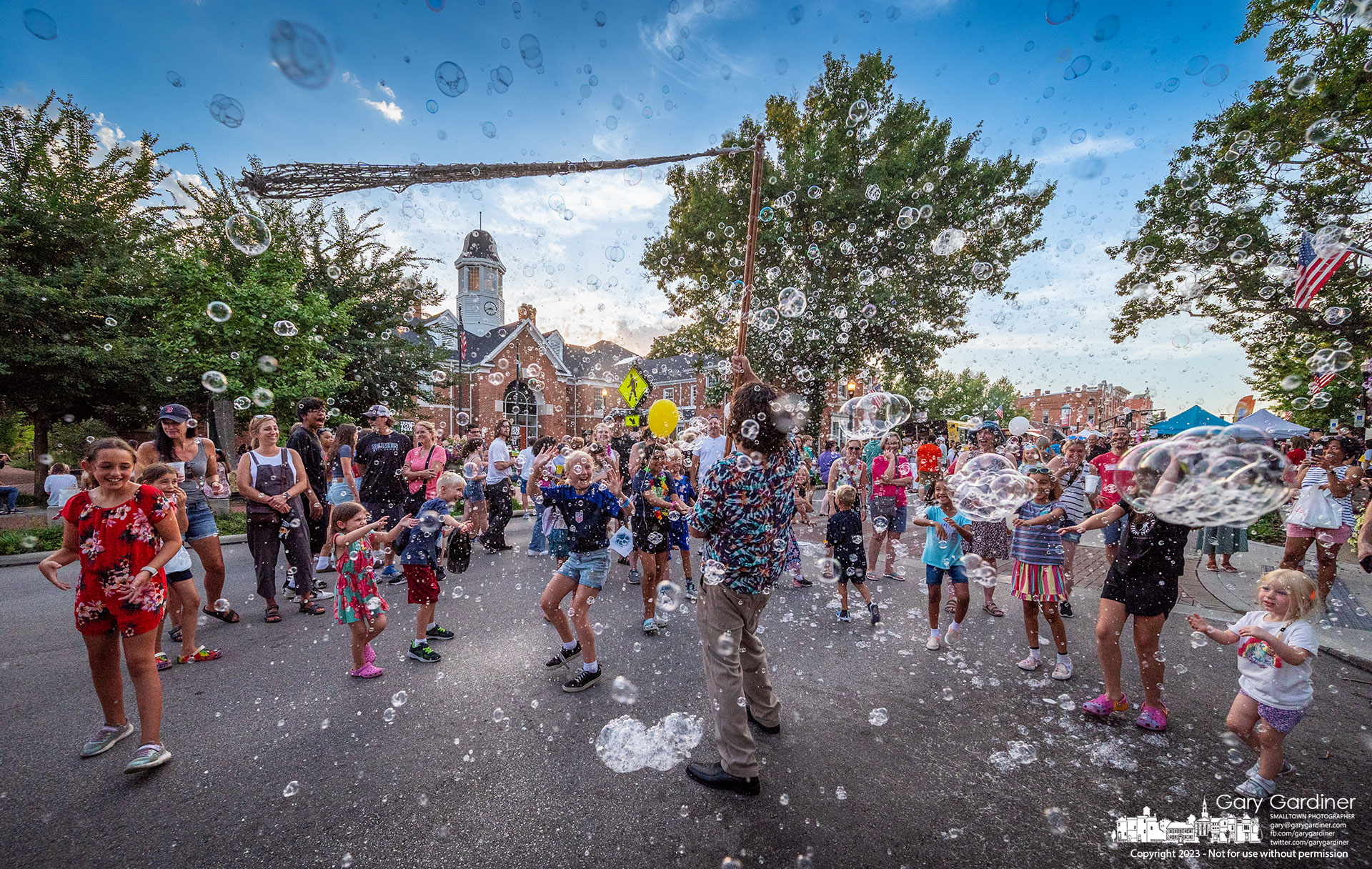A crowd of kids delight in the explosion of bubbles created by The Giant Bubble Maker on his stop in front of city hall during Fourth Friday in Uptown Westerville. My Final Photo for July 28, 2023.